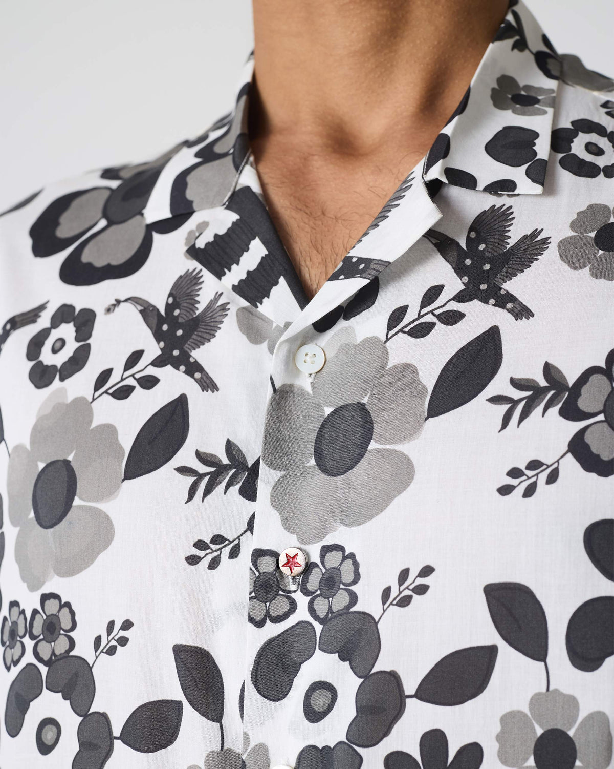 Close-up of a Mistari shirt showing bird and flower motifs and a red star button.