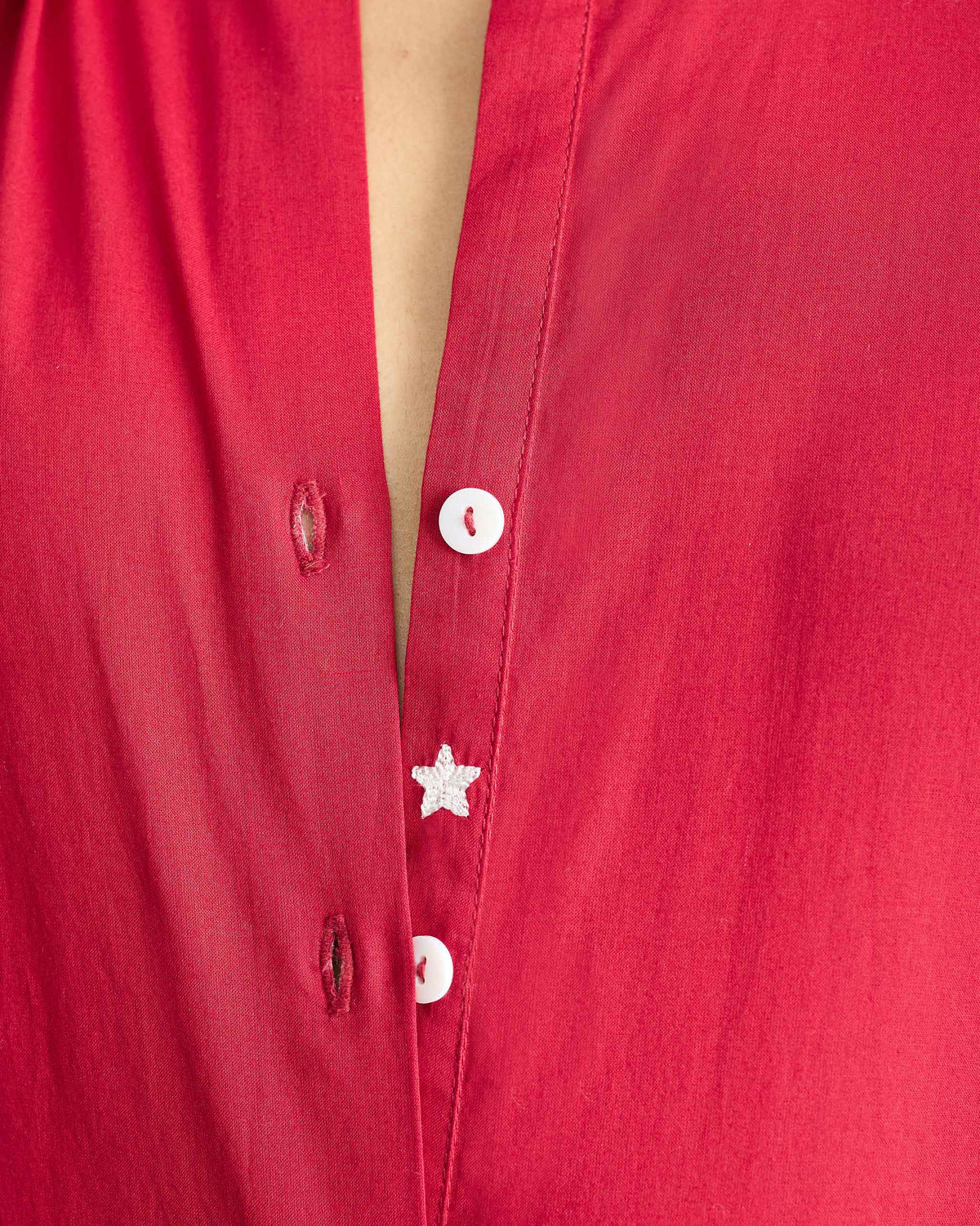 Close-up of a white embroidered star on the placket of a red kurta.