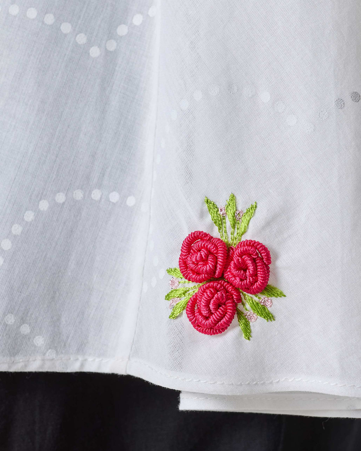 Close-up of red rose embroidery on the hem of a white Ren top.