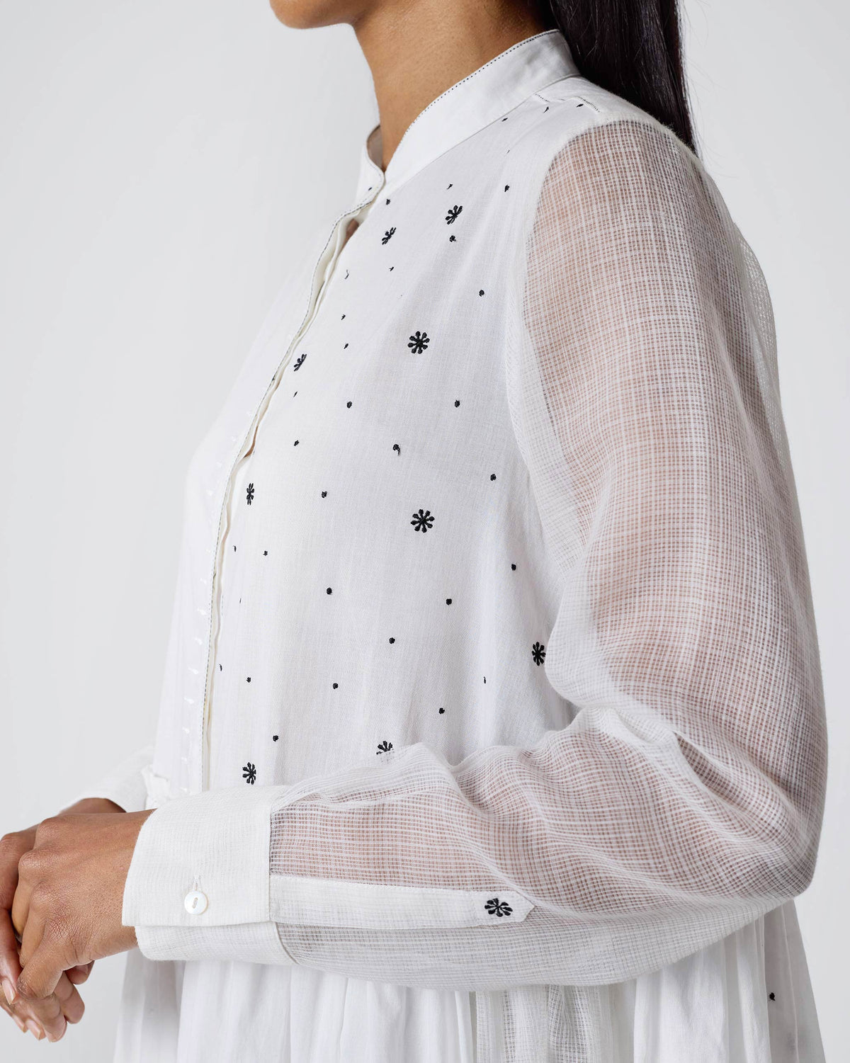 Side view of a white Rayna dress showing sheer sleeves and black embroidered motifs.