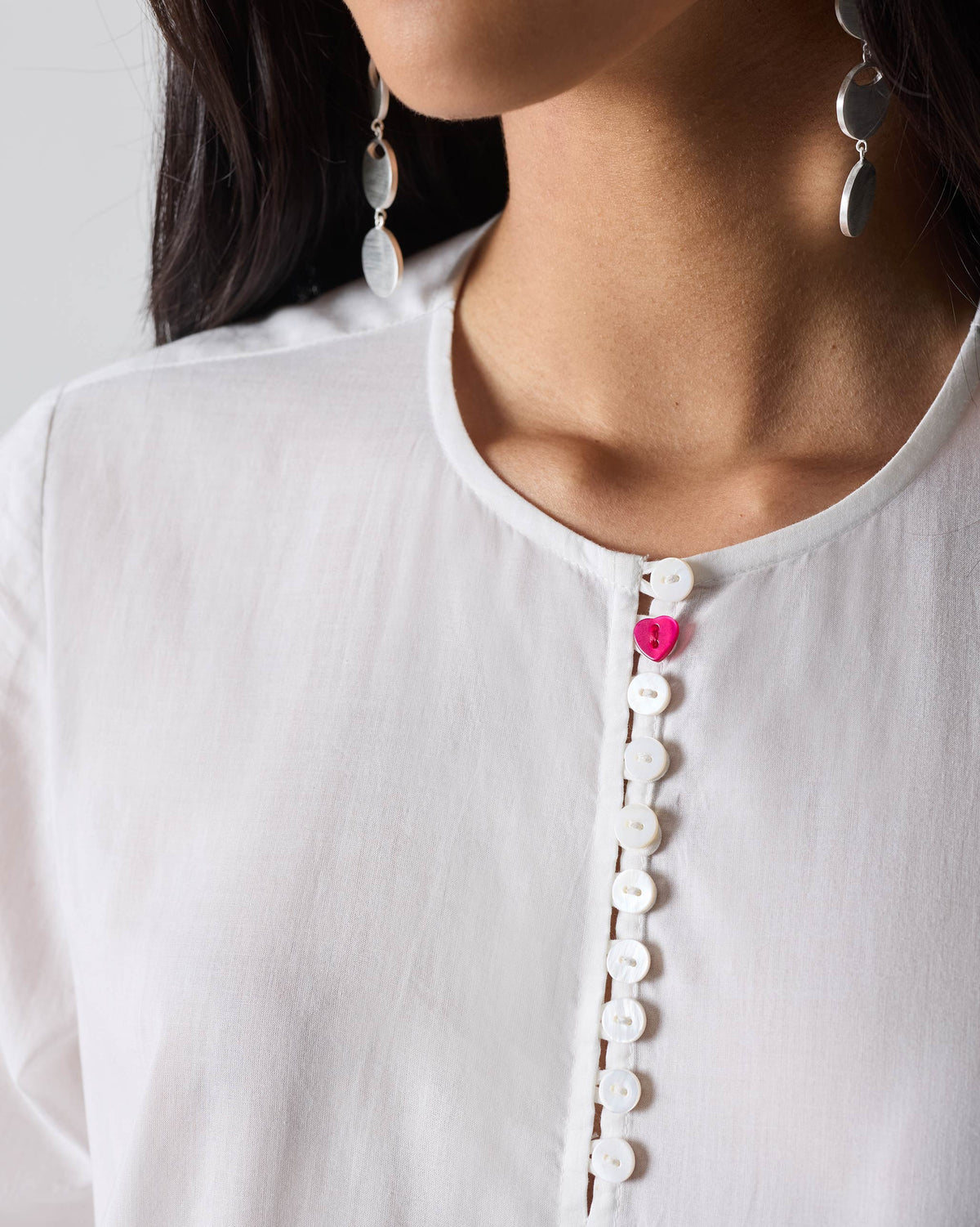 Close-up of the pink heart button on the placket of a white Pleated Waist kurta.