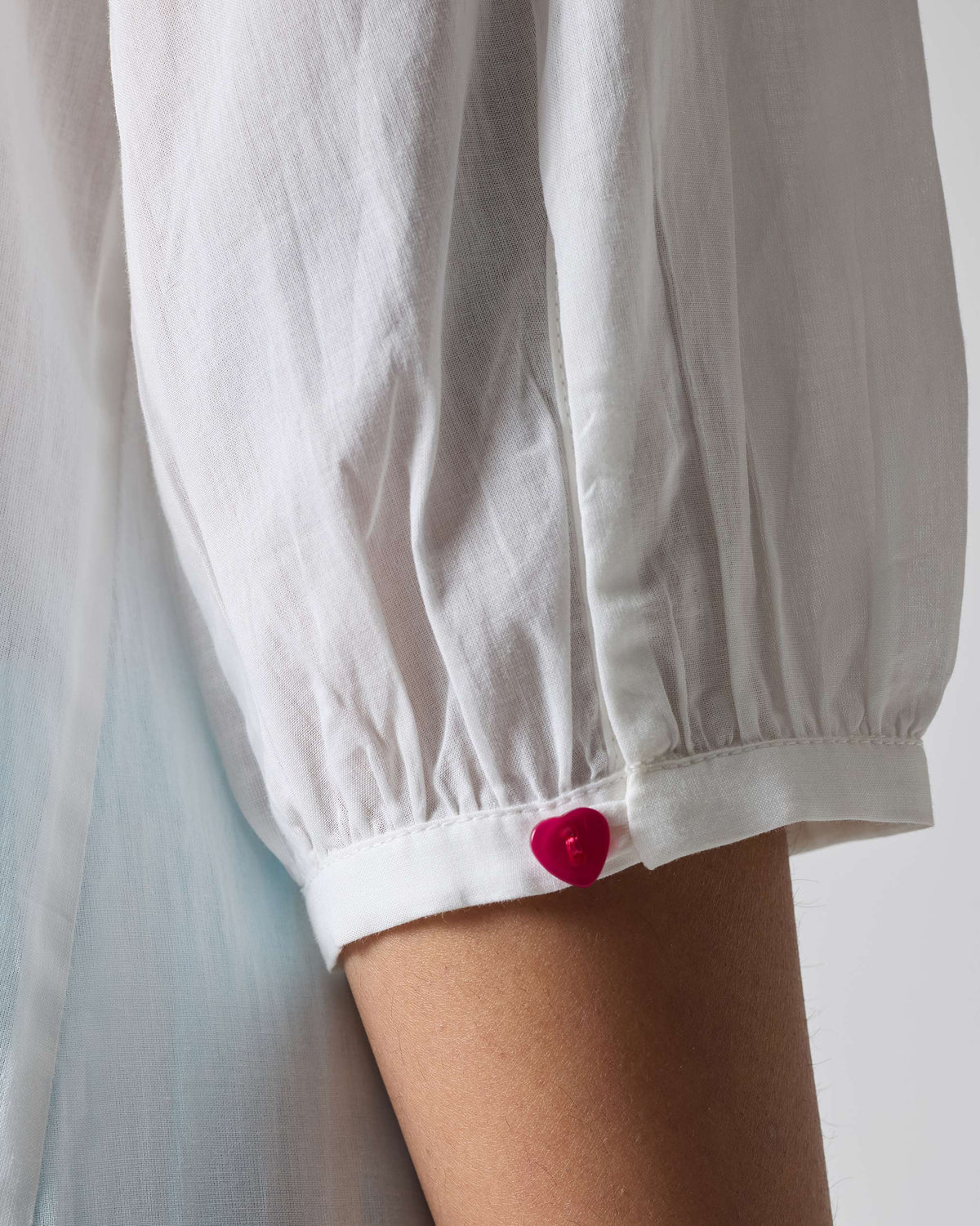 Close-up of a pink heart button on the cuff of a white Pleated Waist kurta.