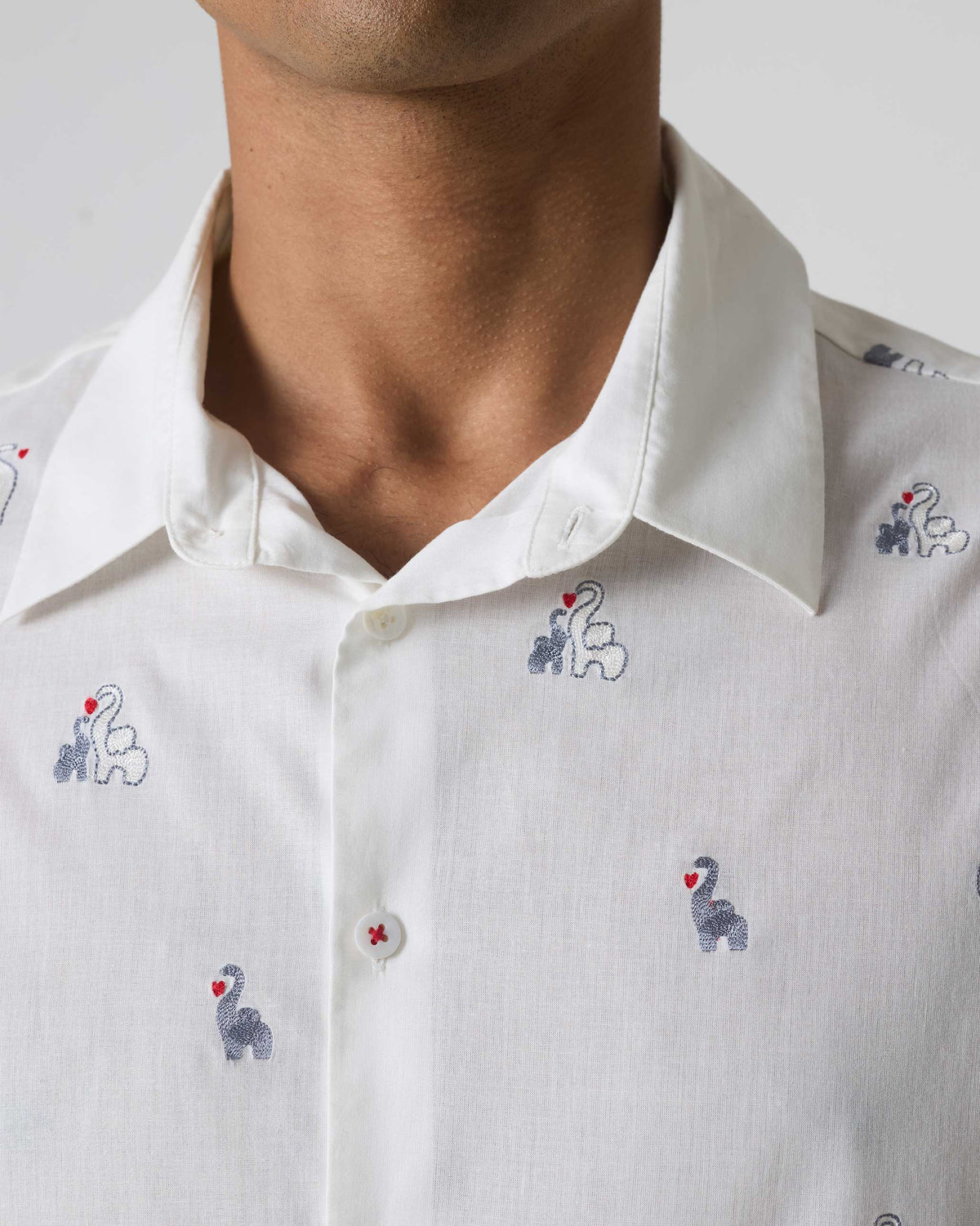 Close-up of a white half sleeves shirt showing grey elephant embroidery and a red-stitched button.