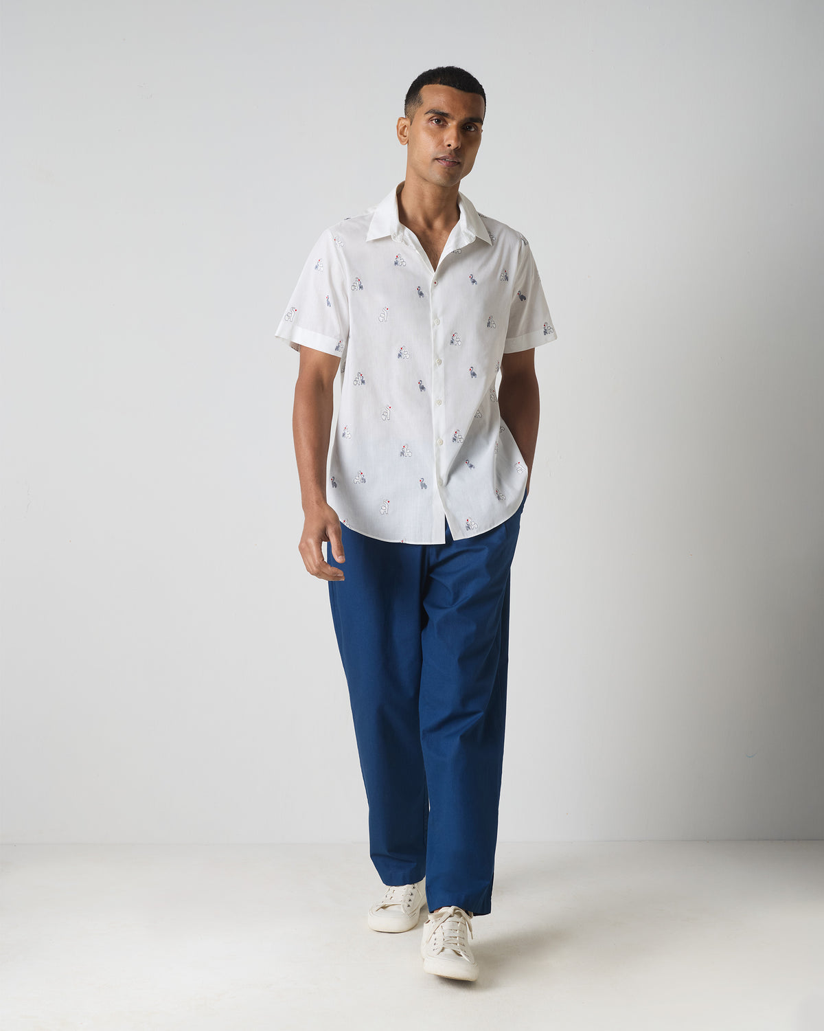 Person wearing a white half sleeves shirt with grey embroidery, shown full length.
