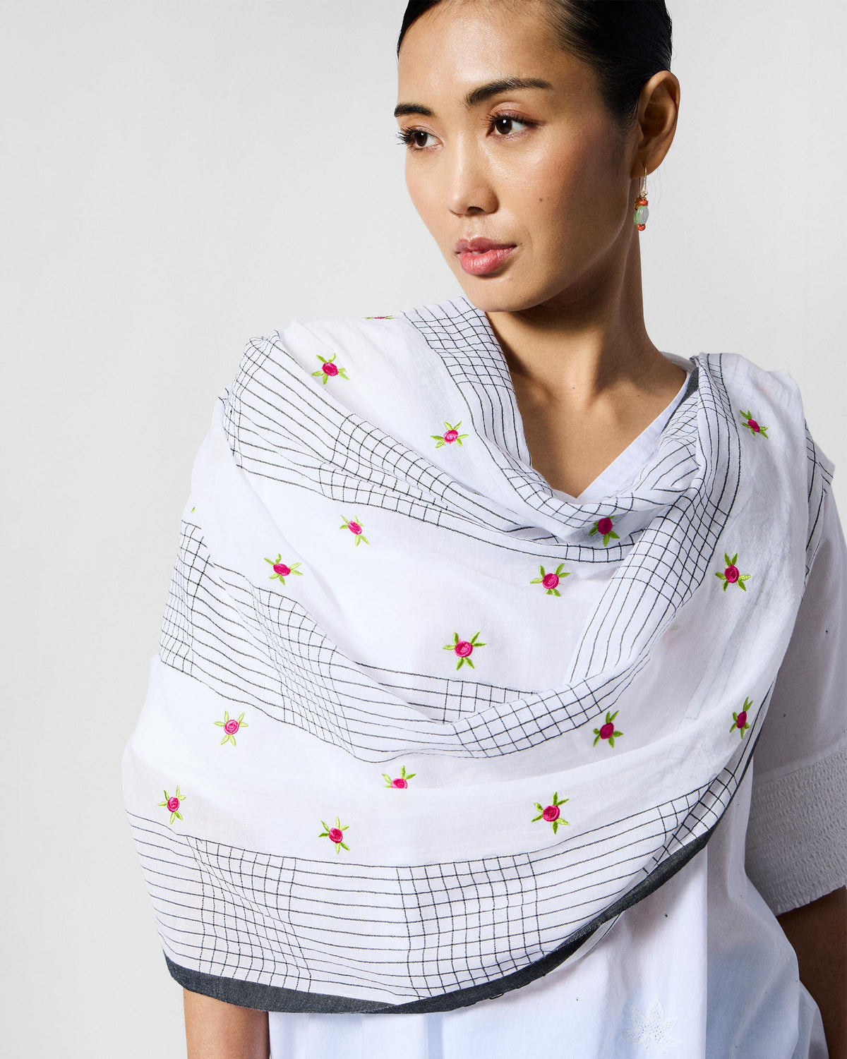 Person wearing a white Rose Bloom scarf with black grid lines and pink roses.