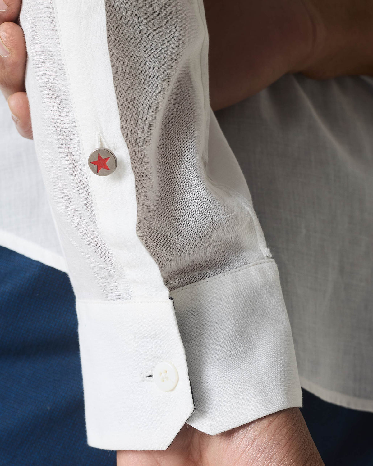 Close-up of a white Neil shirt cuff with a red star button.