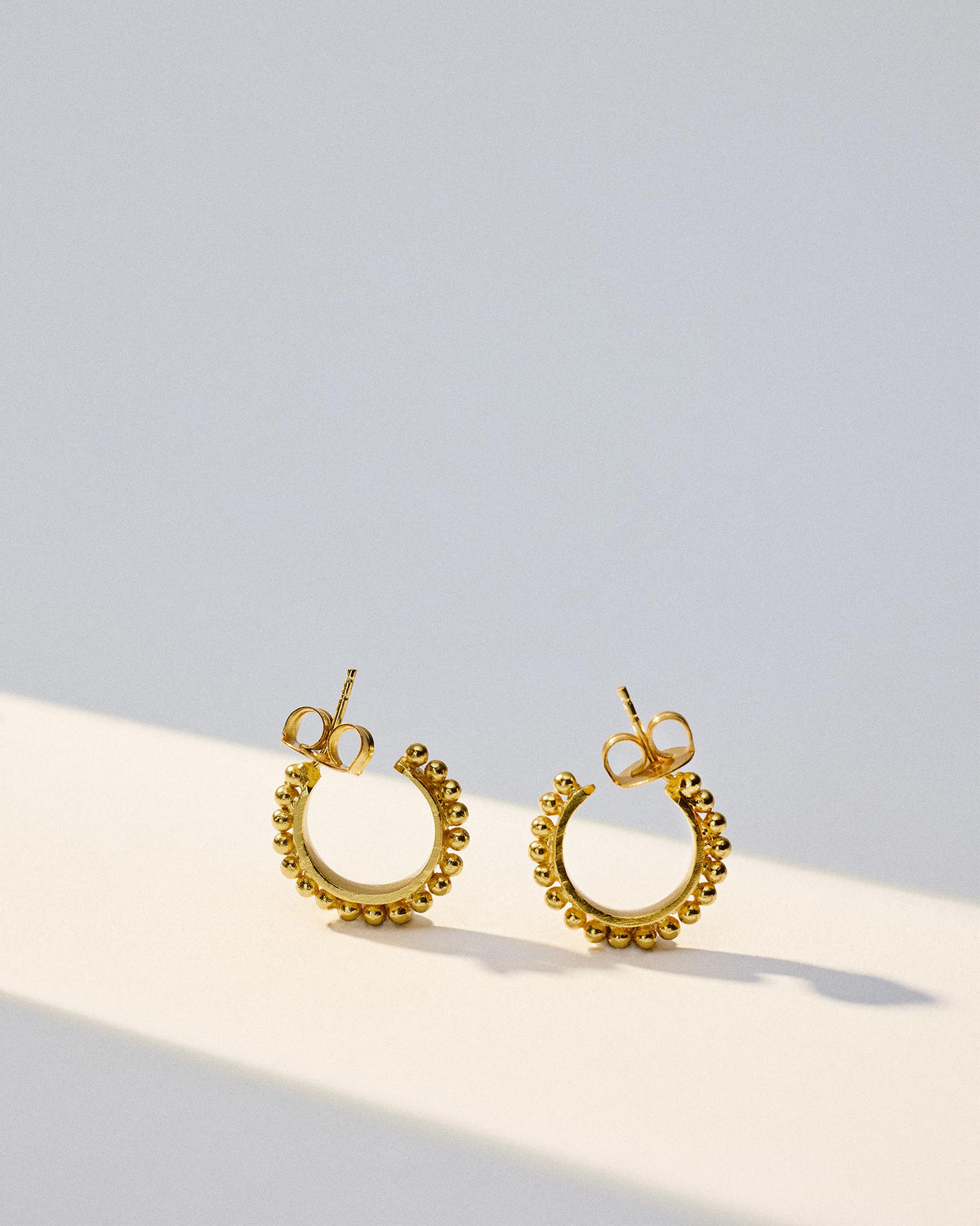 Pair of gold Rava Hoops Small with beaded edges laid flat.