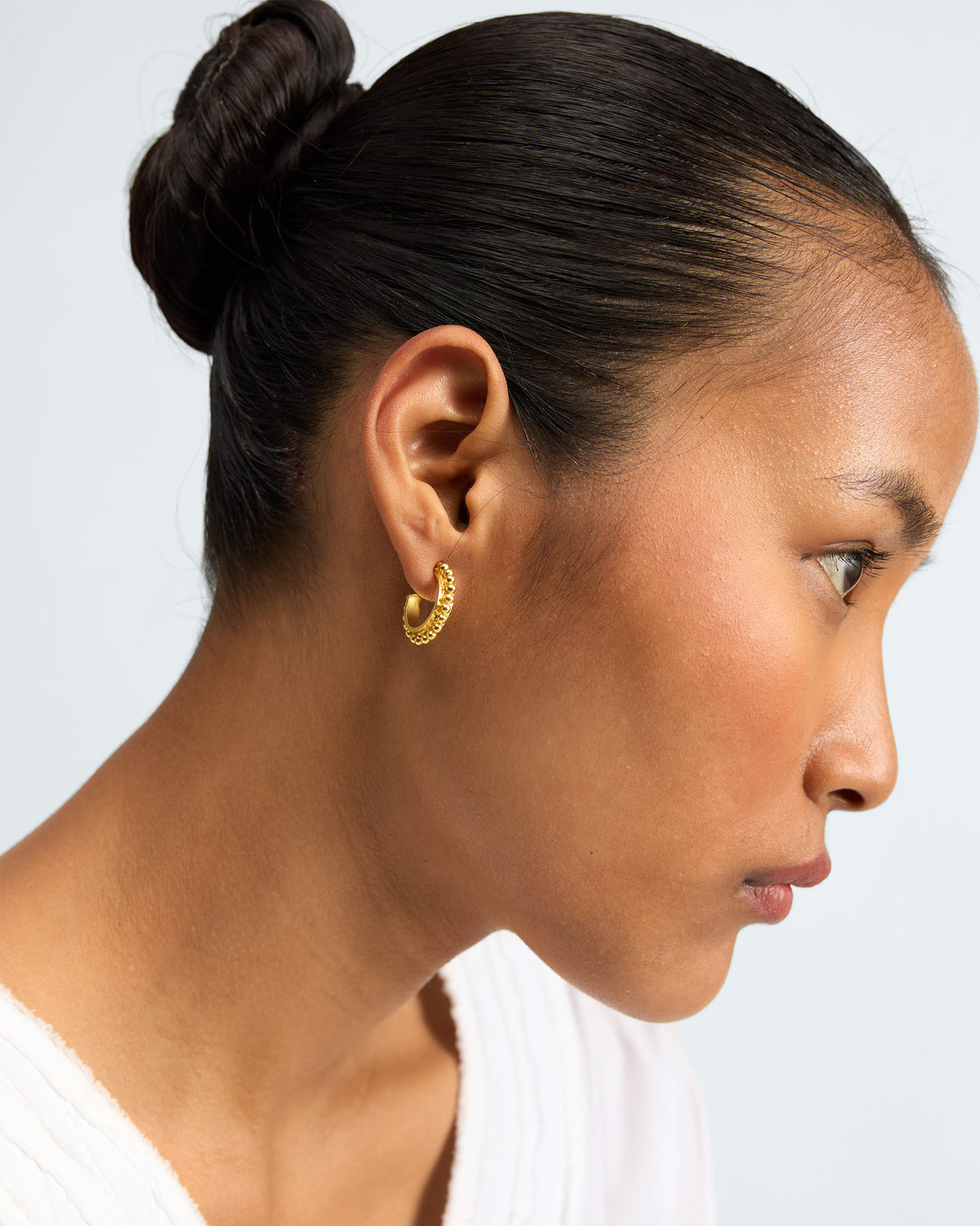 Person wearing a small gold Rava Hoop with a textured edge.
