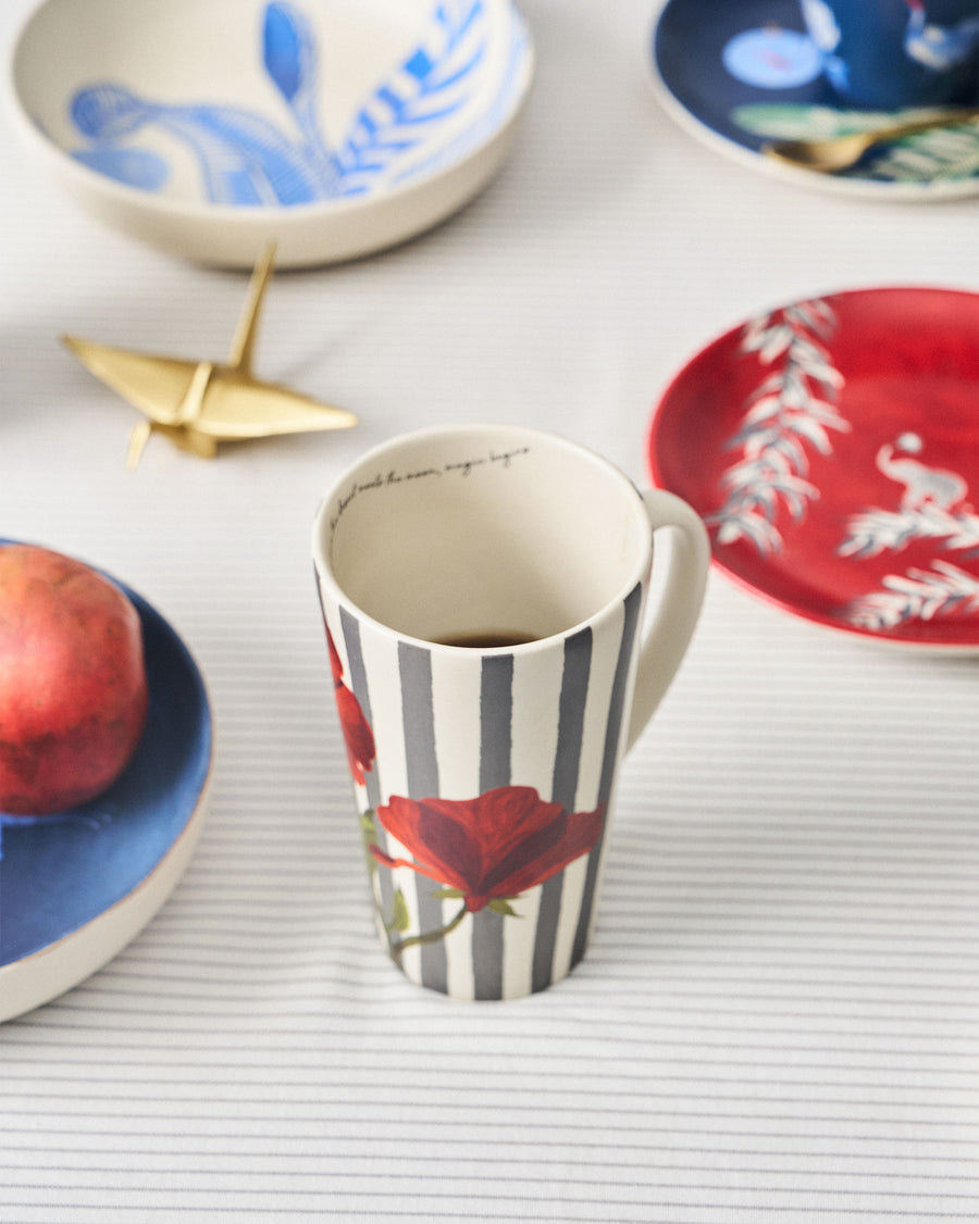 The Striped Poppy mug among blue and red plates on a striped cloth