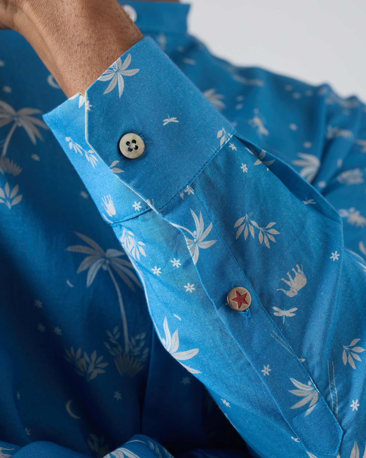 Close-up of a red star cuff button on a blue Nawab shirt.
