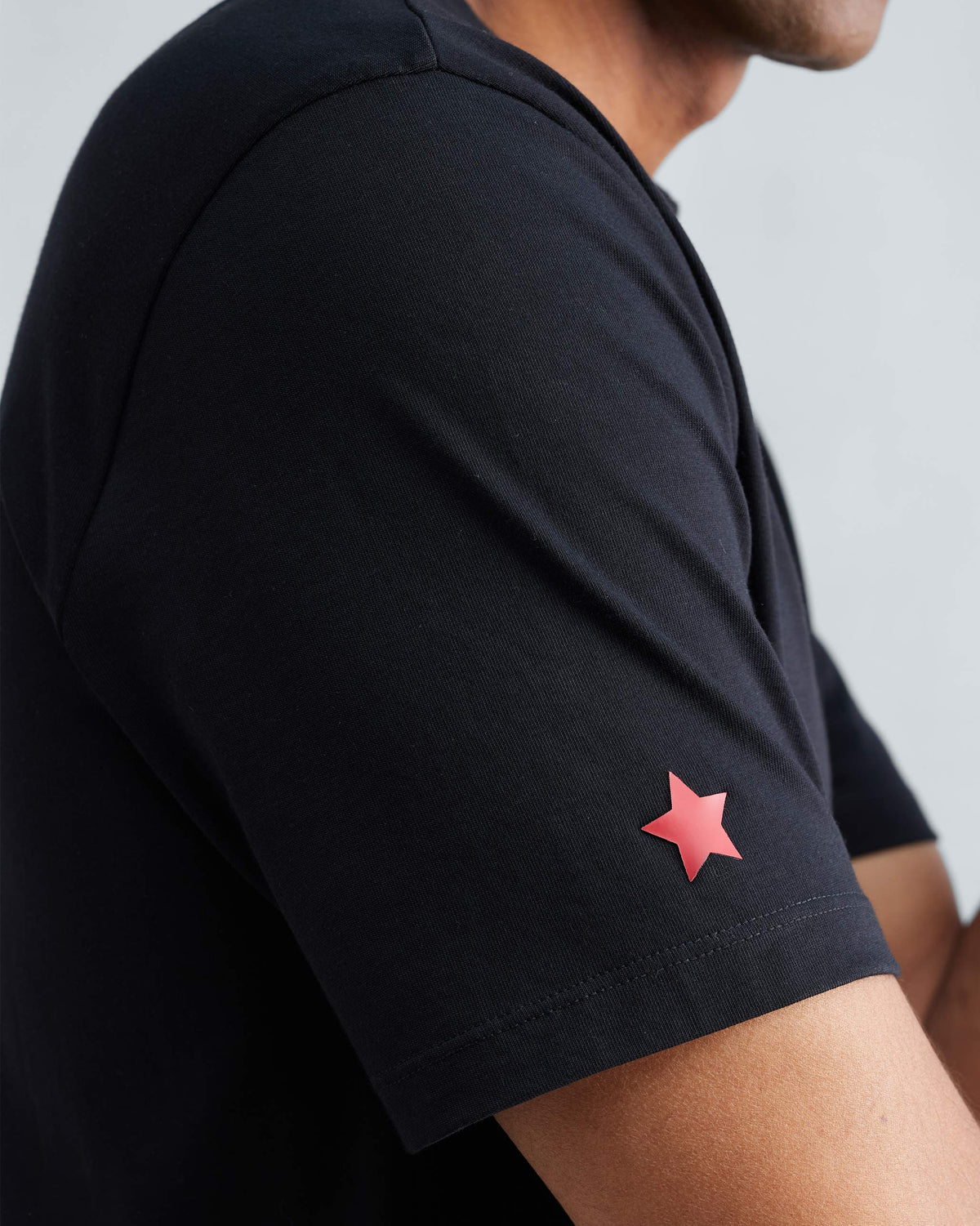 Close-up of a black Everyday T-shirt sleeve showing a red star detail.