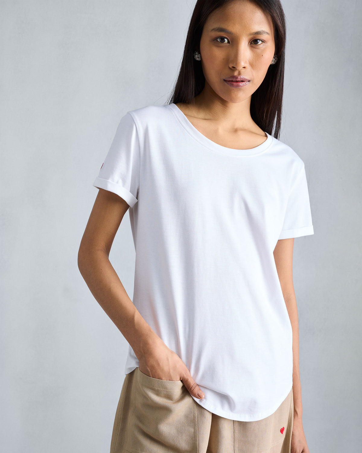 Person wearing a white Basic T-Shirt with a red heart on the sleeve.