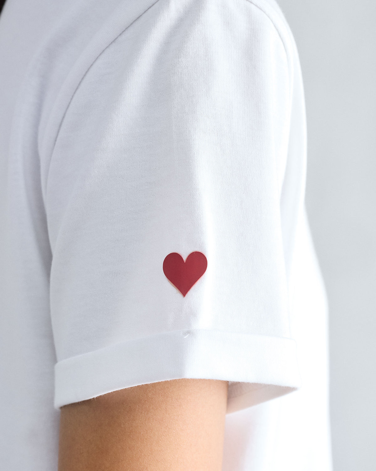 Close-up of a red heart embroidery on a white Basic T-Shirt sleeve.