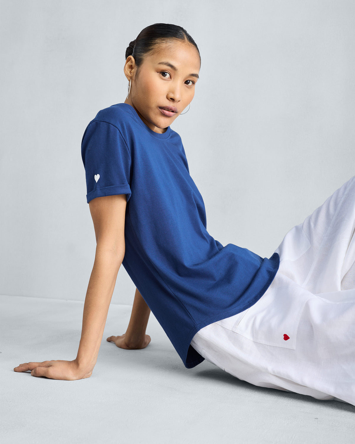 Person wearing a navy Basic T-Shirt with a white heart on the sleeve.