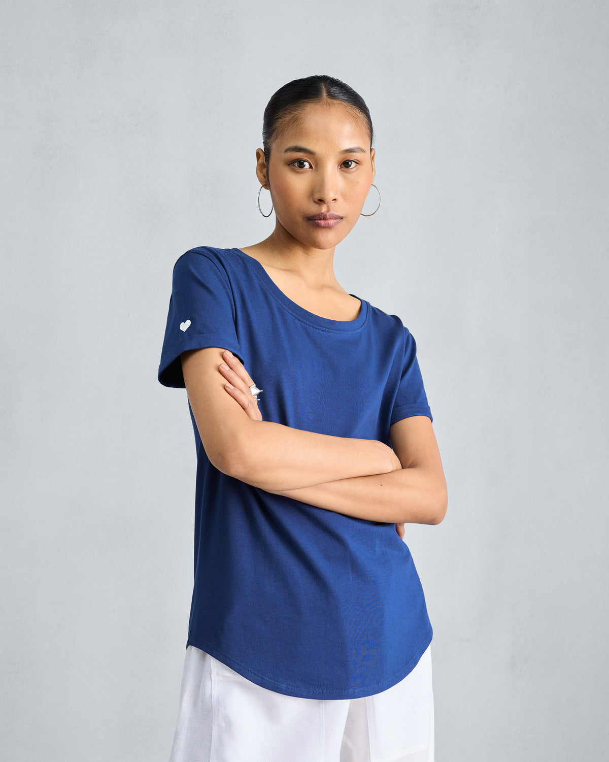 Person wearing a navy crew-neck Basic T-Shirt with a white sleeve heart.