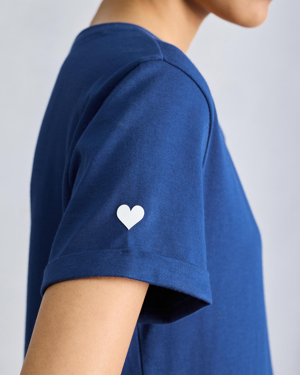 Close-up of a white heart embroidery on a navy Basic T-Shirt sleeve.