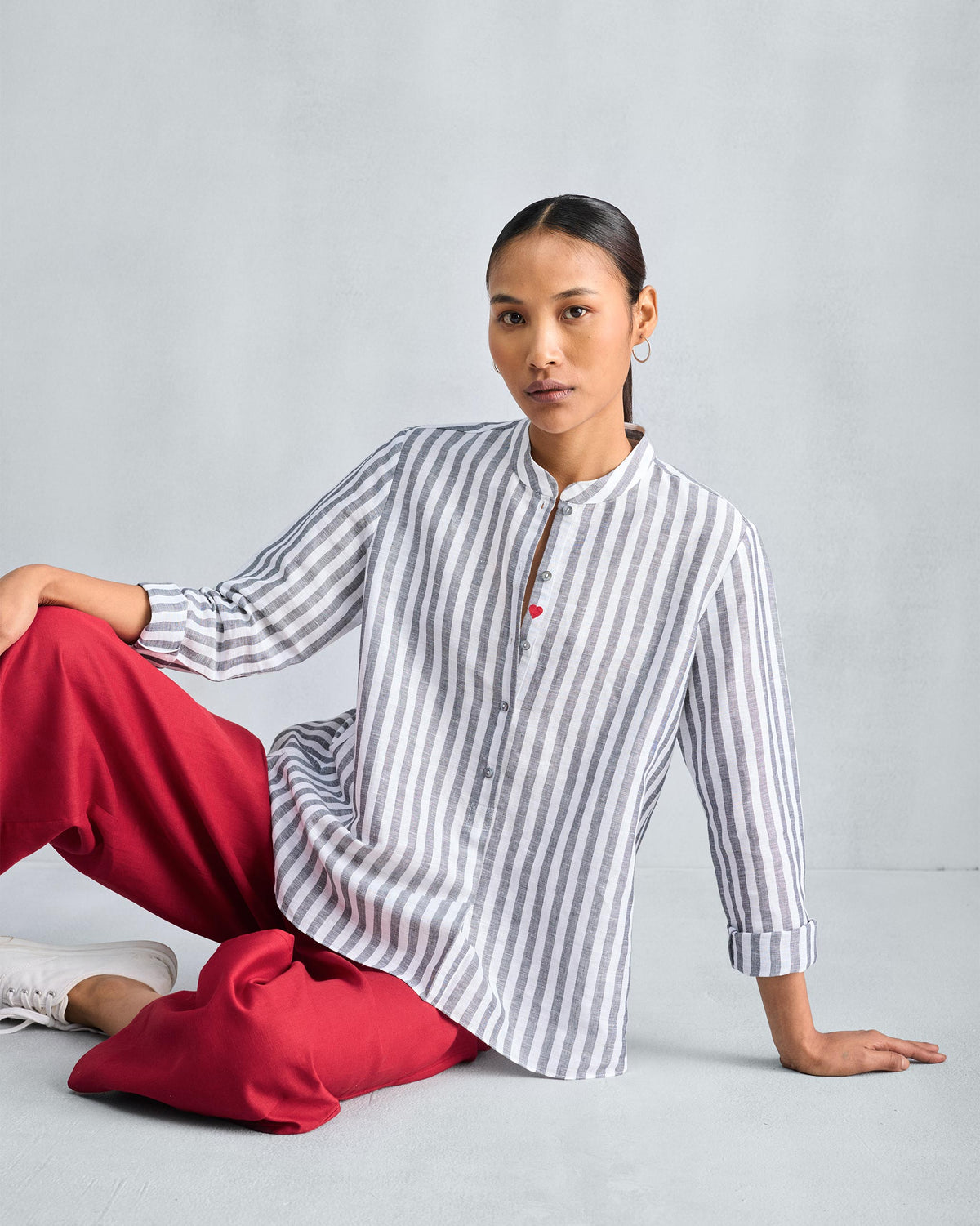 Person wearing a charcoal striped mandarin collar top with a red heart.