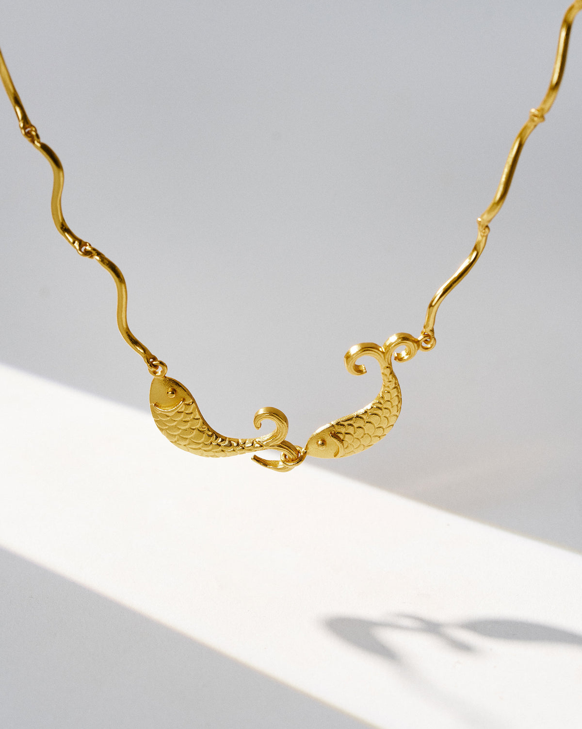 Close-up of twin fish motif on a gold Meen necklace.
