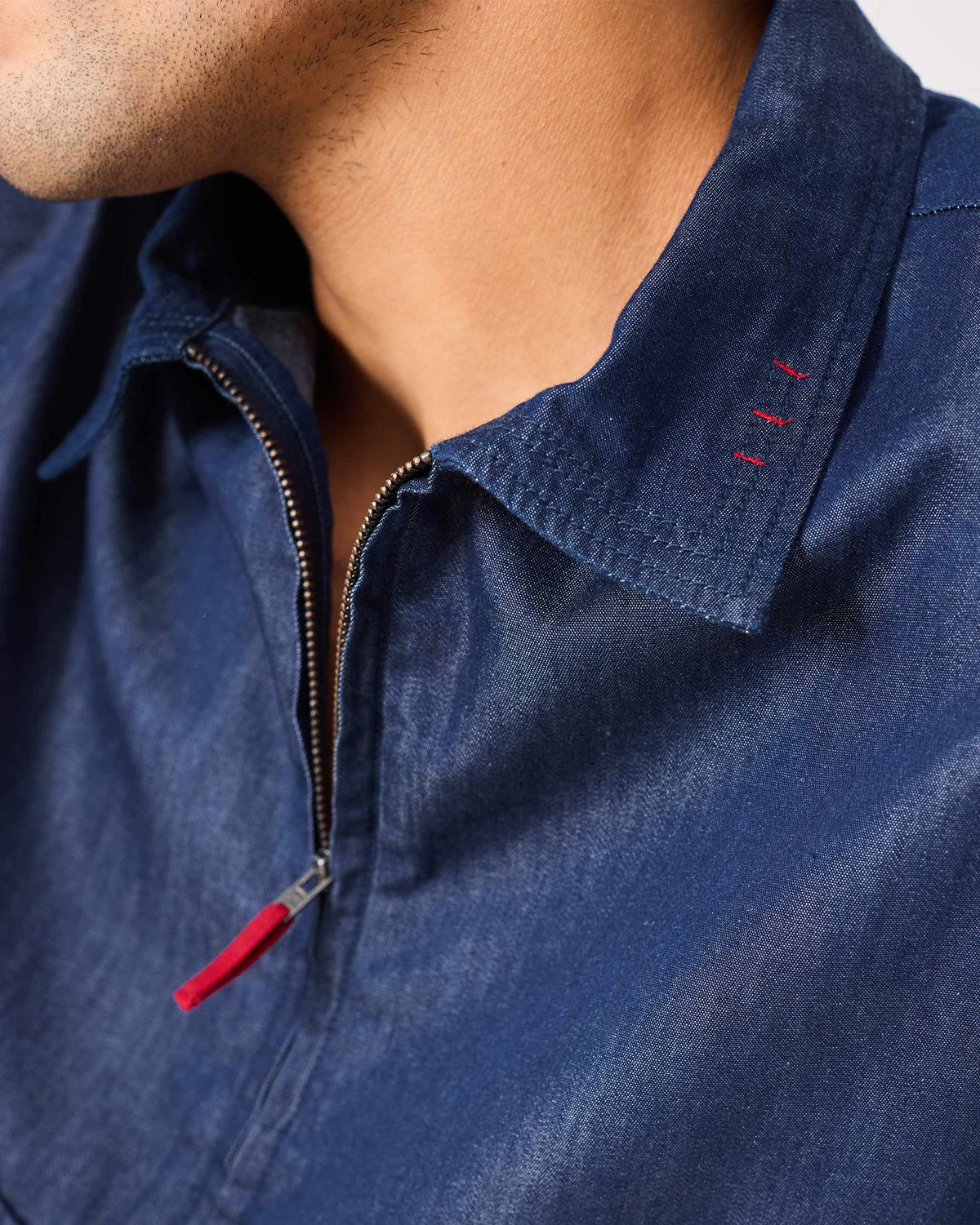 Close-up of a denim Konbini Shirt showing a red zipper pull and collar stitches.