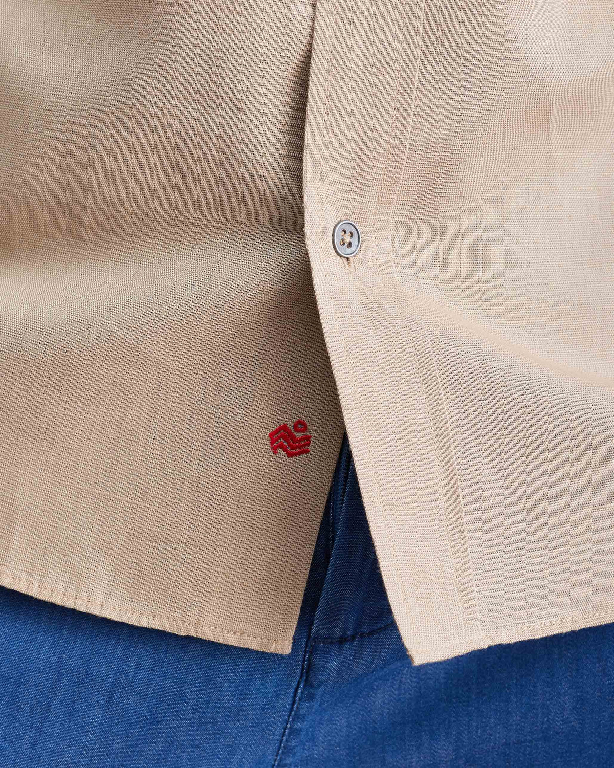 Close-up of a red logo near the hem of a beige half sleeve shirt.
