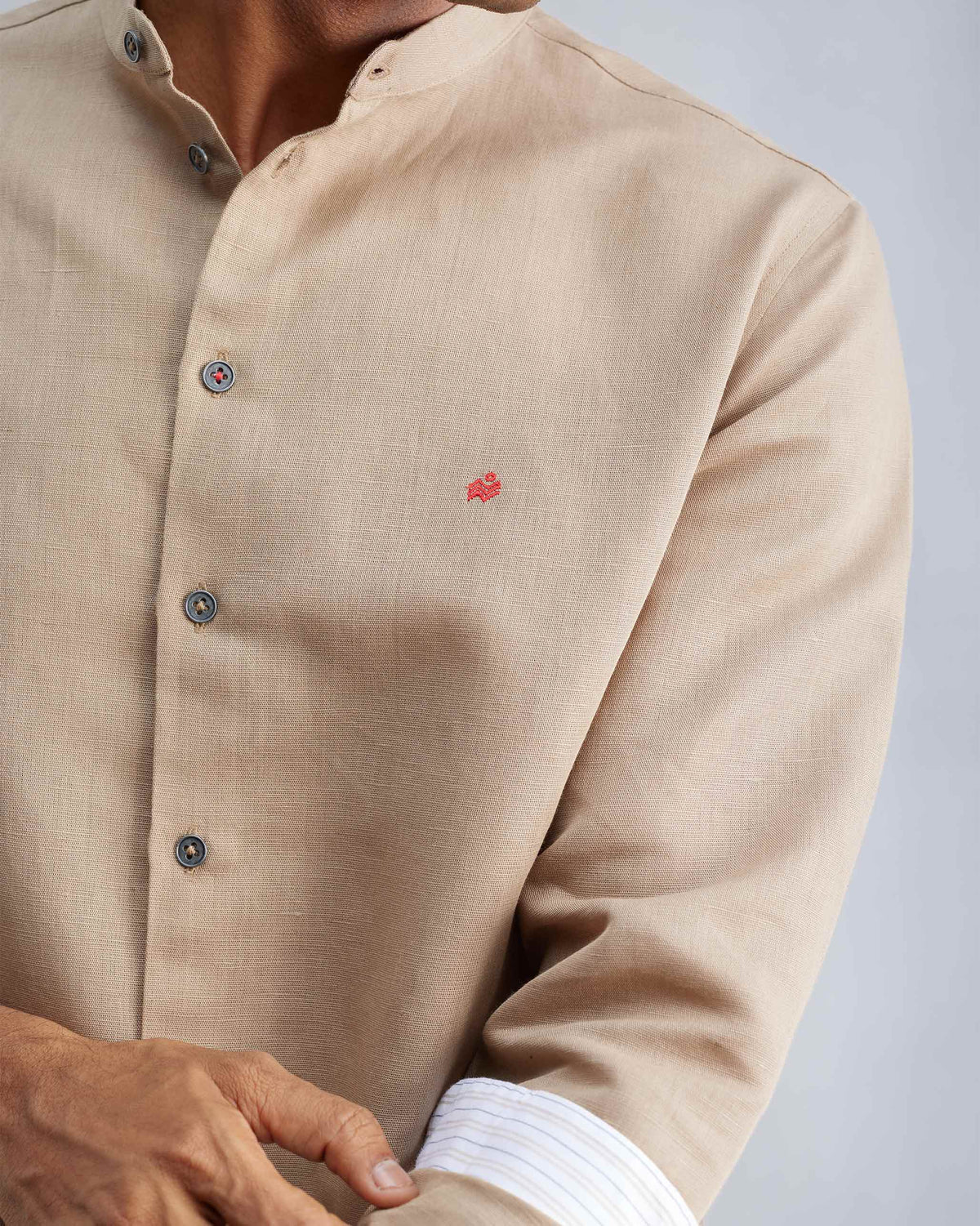 Close-up of a beige Nawab shirt showing the red logomark and striped cuff trim.