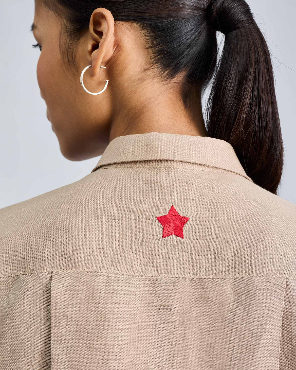 Close-up of a red embroidered star on the back of the beige drop armhole shirt.