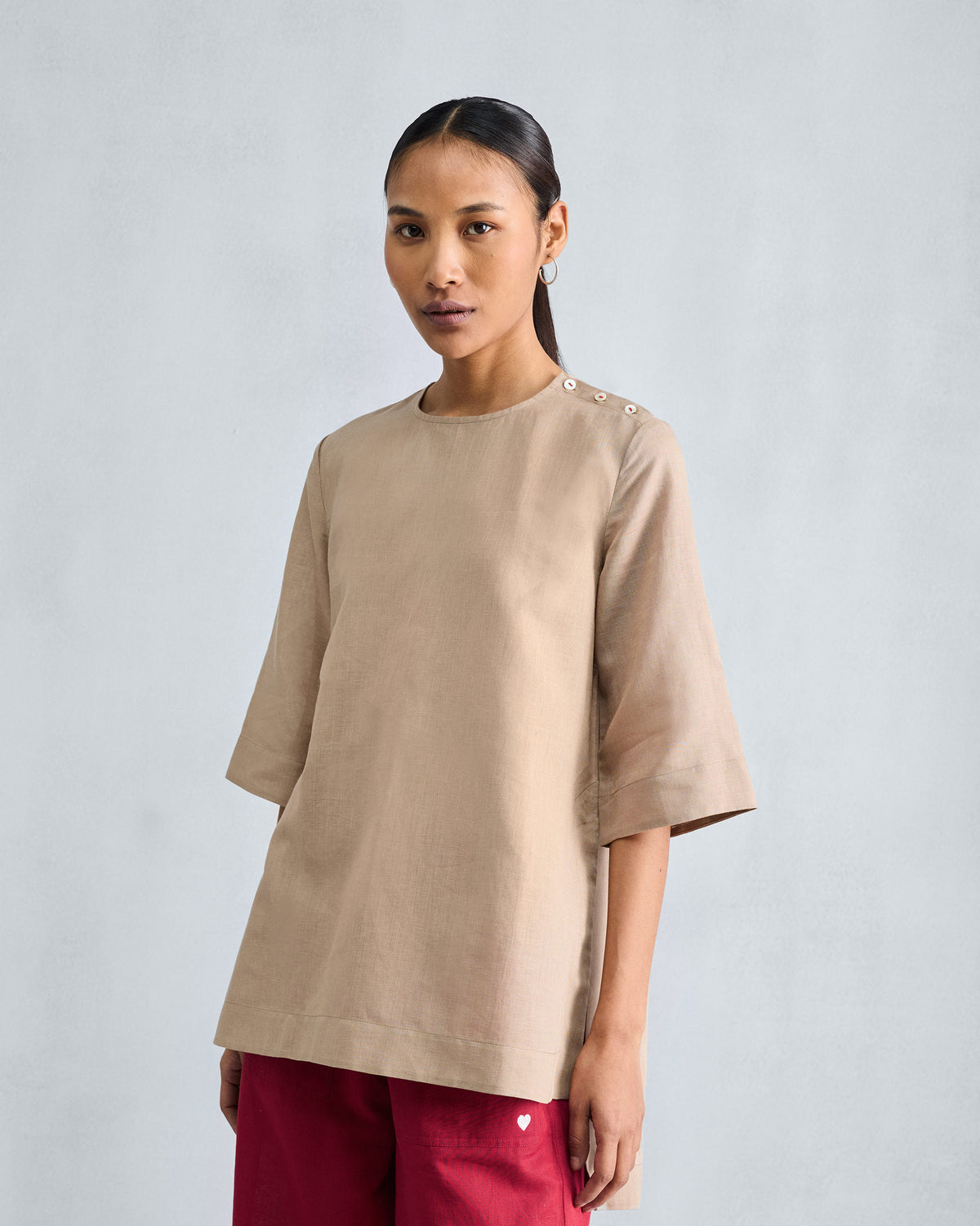 Person wearing a beige High Slit Top with three buttons along the shoulder.