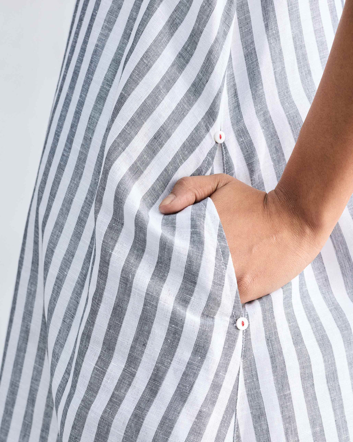Close-up of a side pocket with red-stitched buttons on the striped dress.