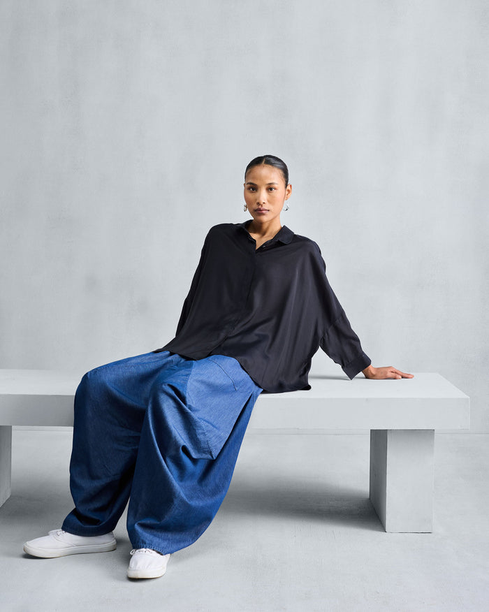 Person wearing a black boxy shirt with a collar, concealed placket, and dropped shoulders.