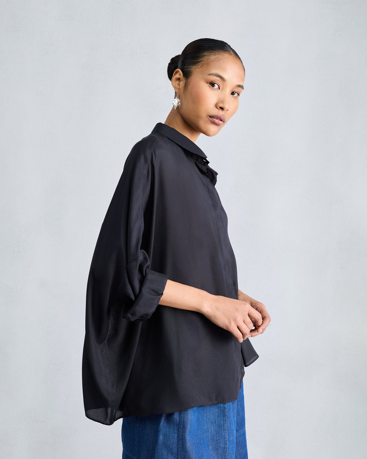 Side view of a black boxy shirt showing dropped shoulders and loose drape.
