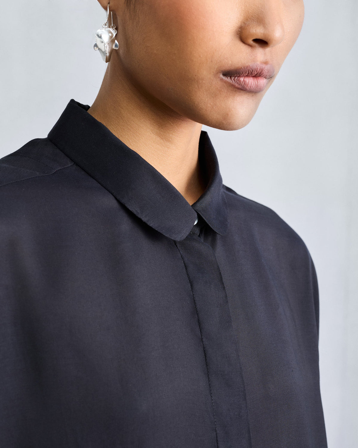 Close-up of the rounded collar and concealed placket on a black boxy shirt.