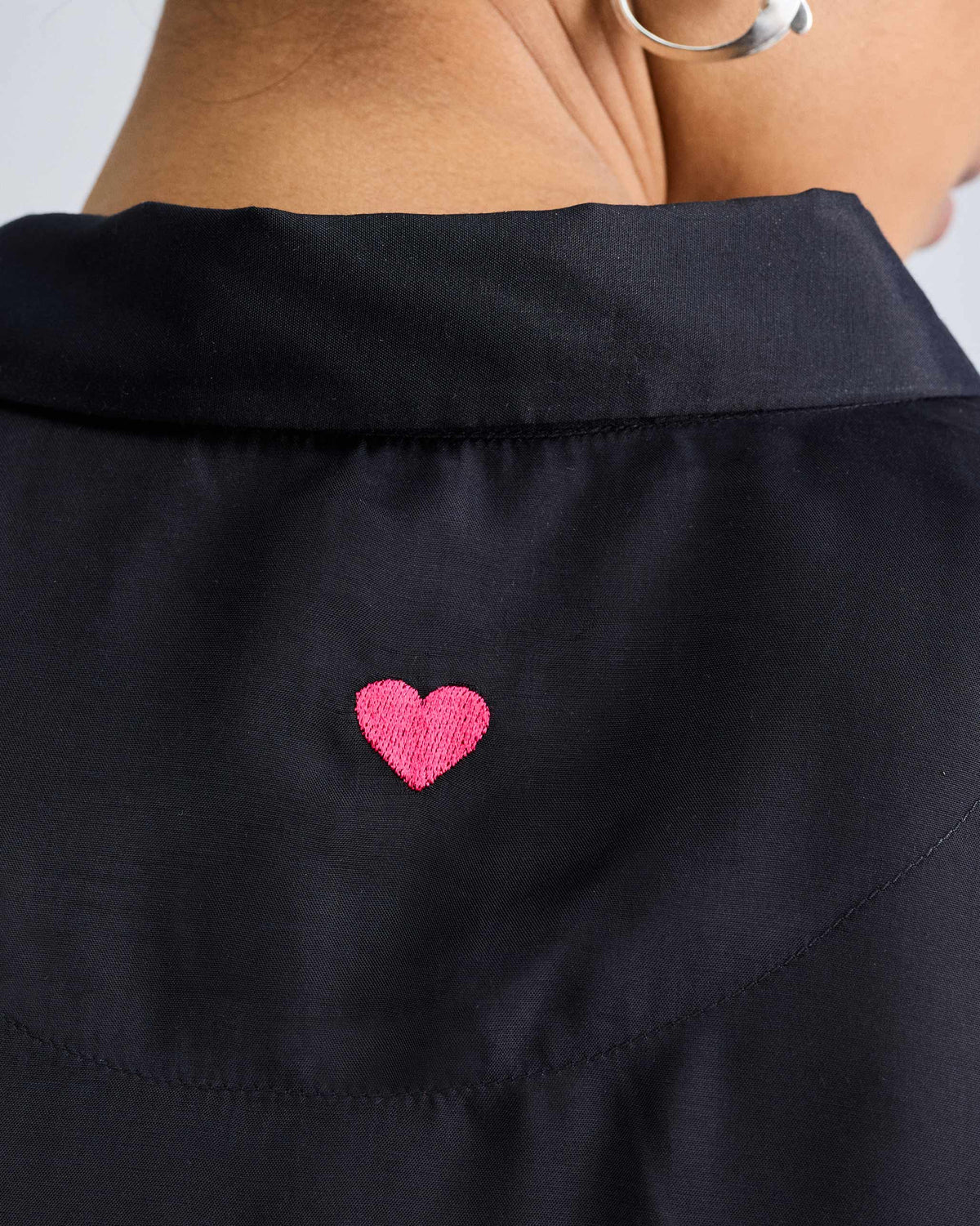 Close-up of a pink embroidered heart on the back of a black boxy shirt.