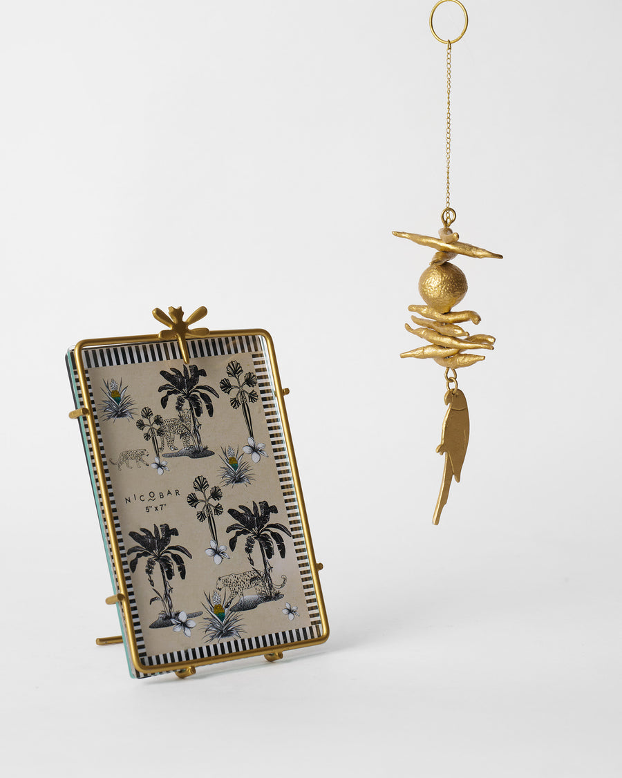 A gold frame with a dragonfly on top beside a gold nimbu-mirchi charm with a parrot