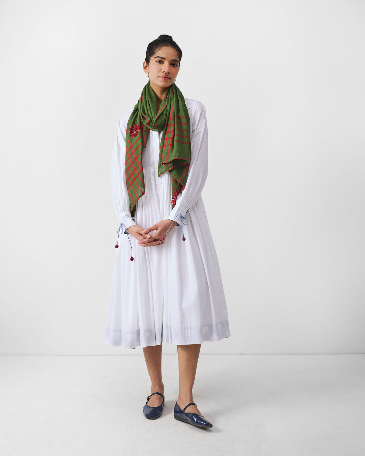 Person in a white Puritsu shirt dress styled with an olive check scarf.