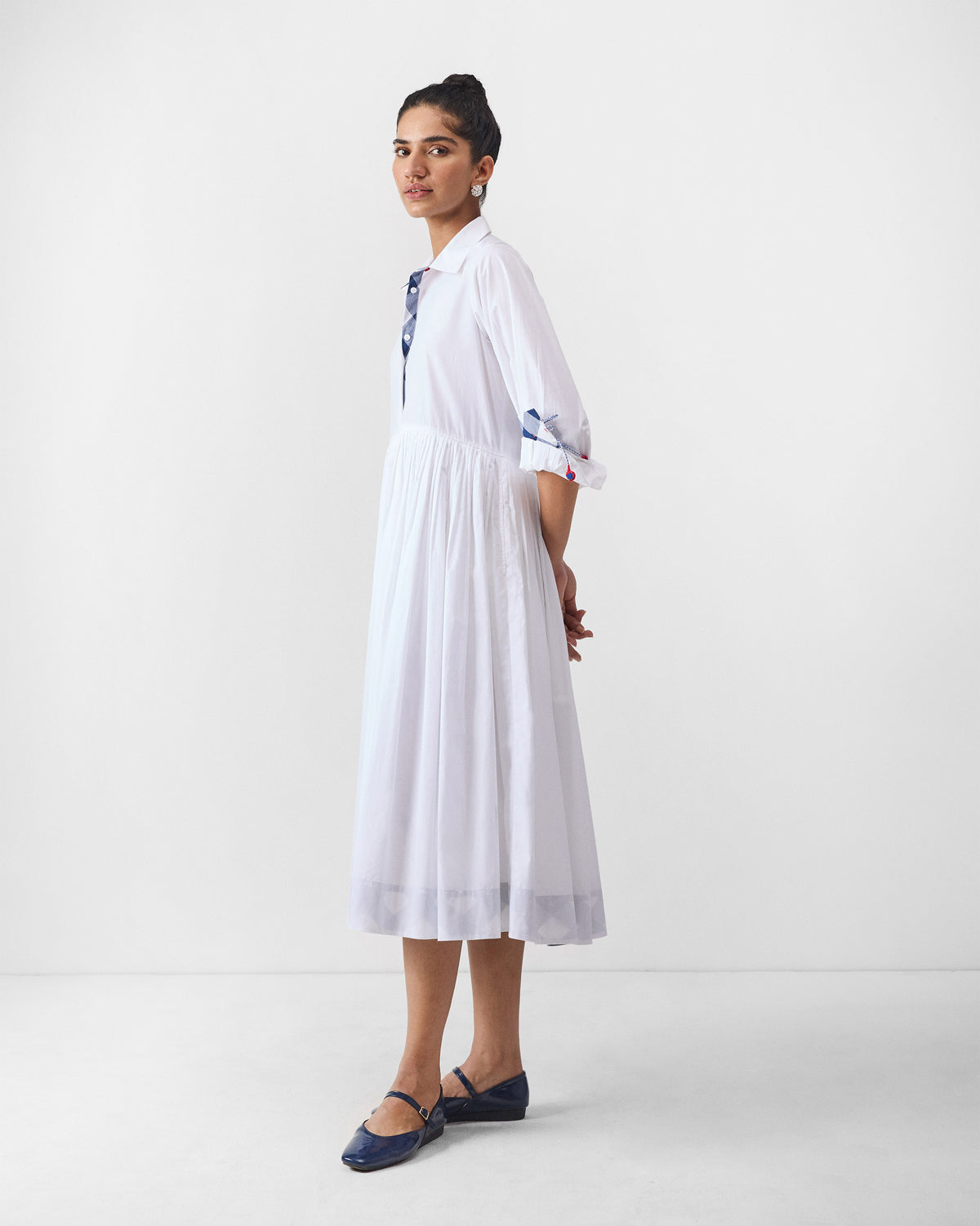 Side view of a white Puritsu shirt dress with a full pleated skirt.