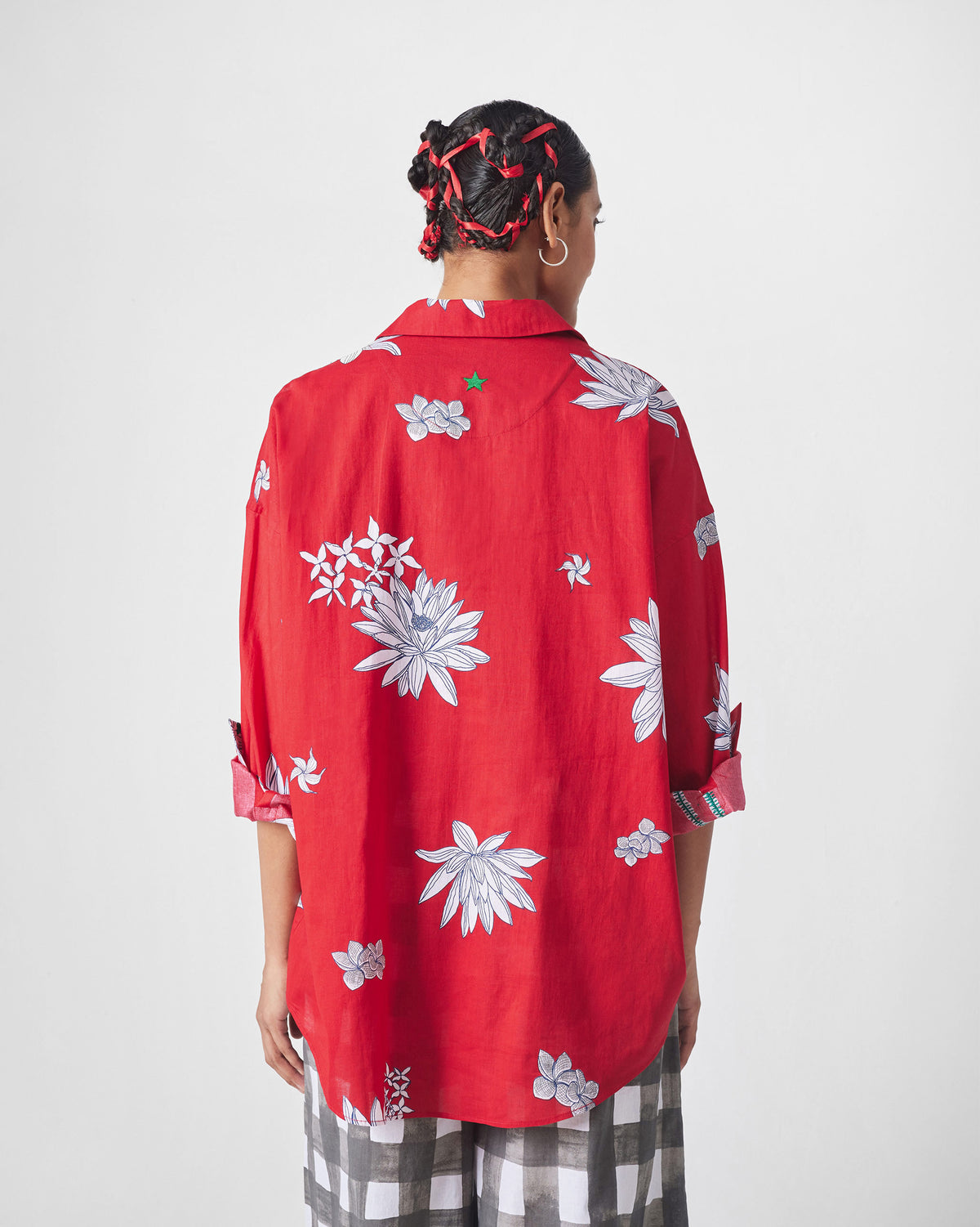 Back of a red oversized shirt with white flowers and a green embroidered star.