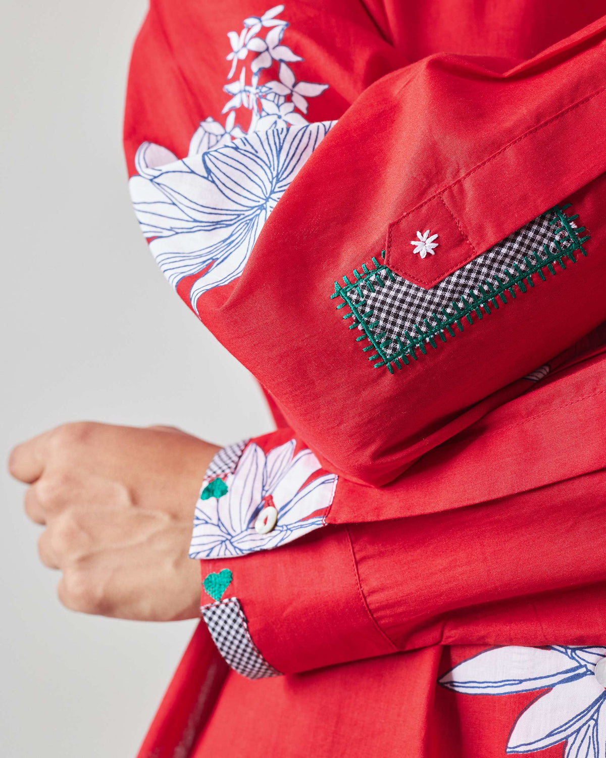 Close-up of a gingham patch and green stitching on the red oversized shirt sleeve.