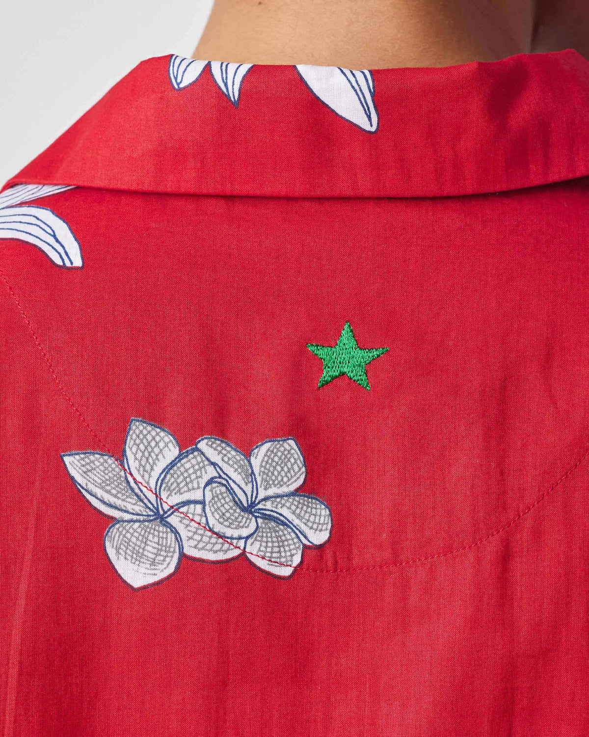 Close-up of a green embroidered star on the back of the red oversized shirt.