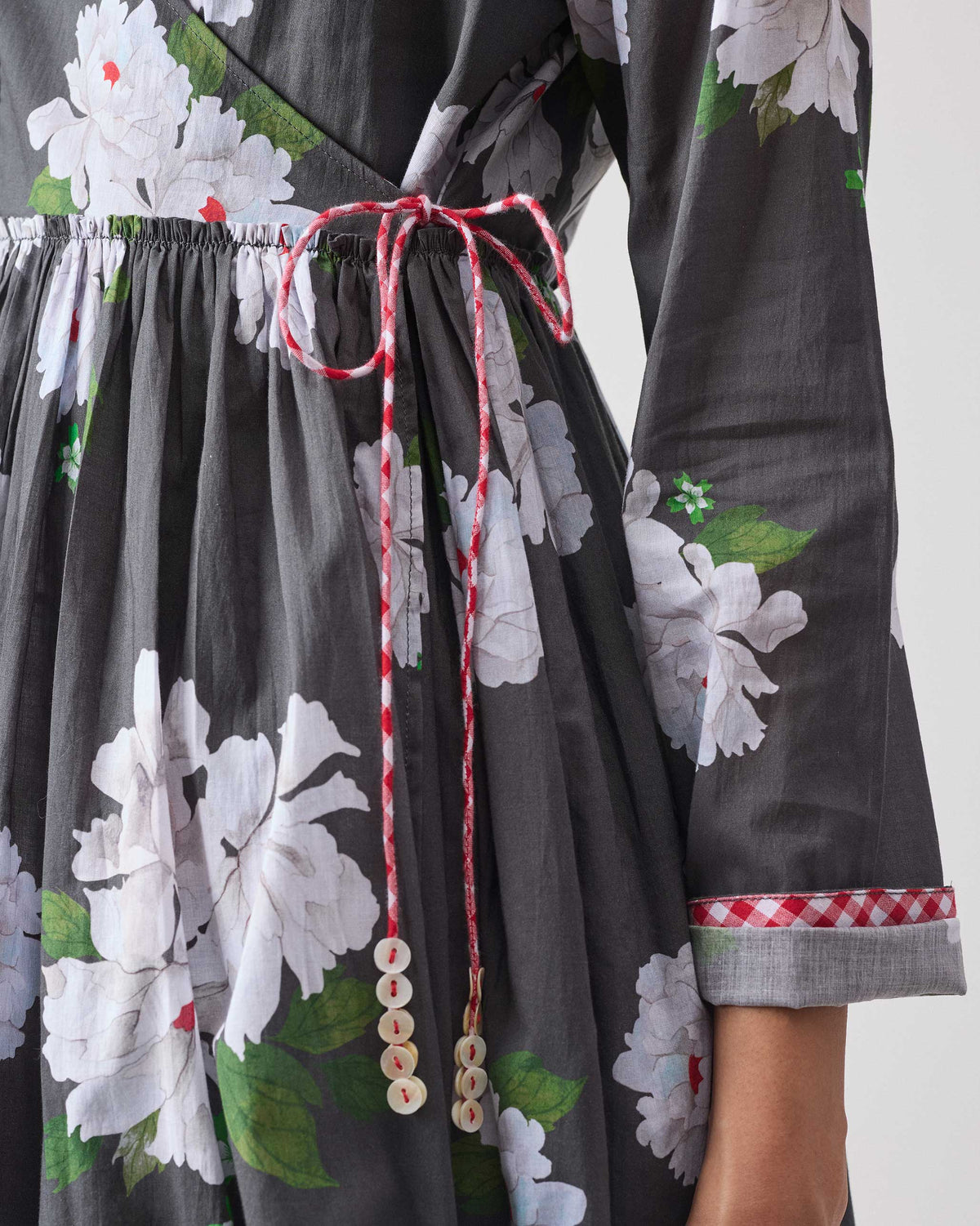 Close-up of a charcoal floral angrakha with a red and white side tie.