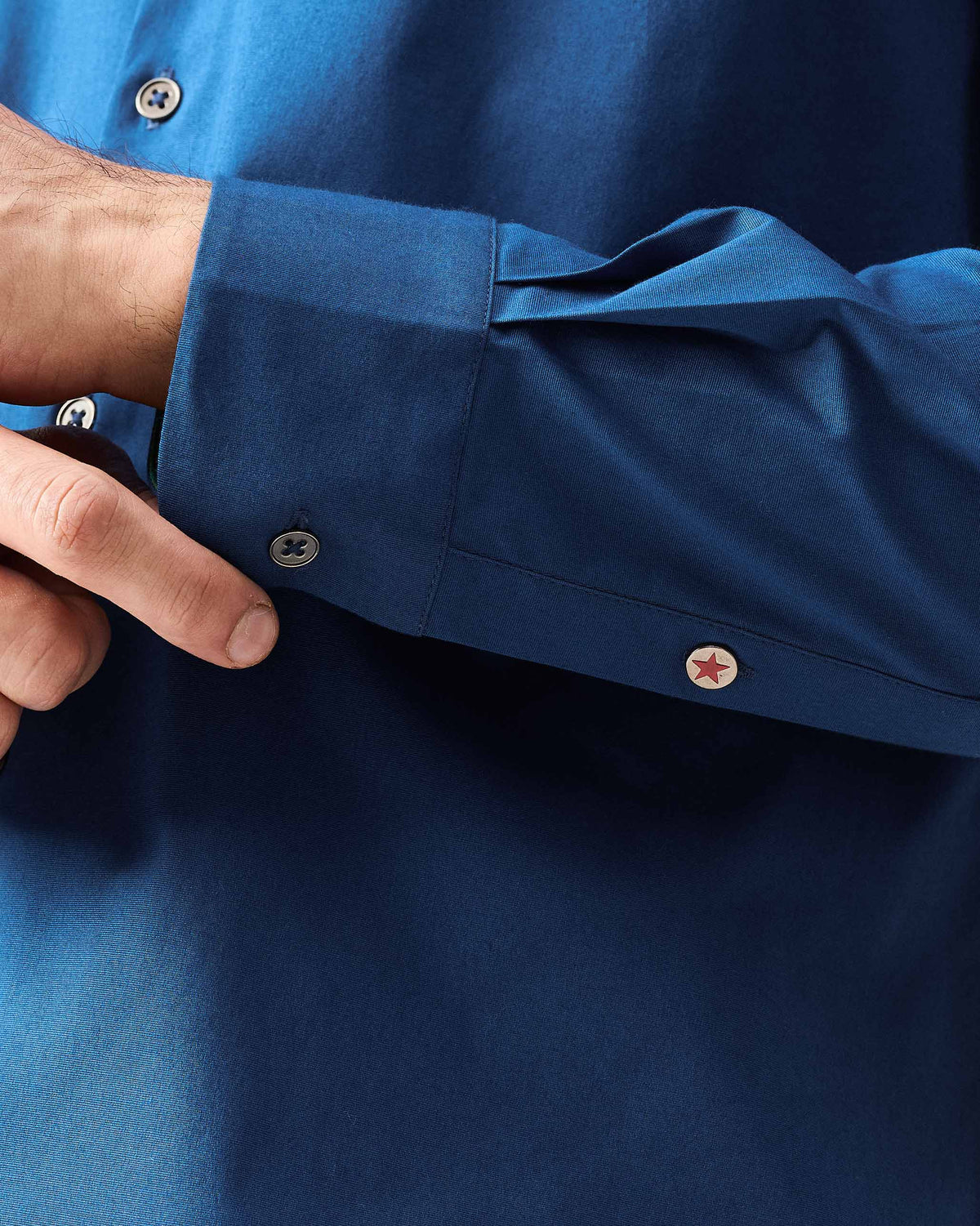 Close-up of a dark blue Hakuna Shirt cuff showing a red star button.