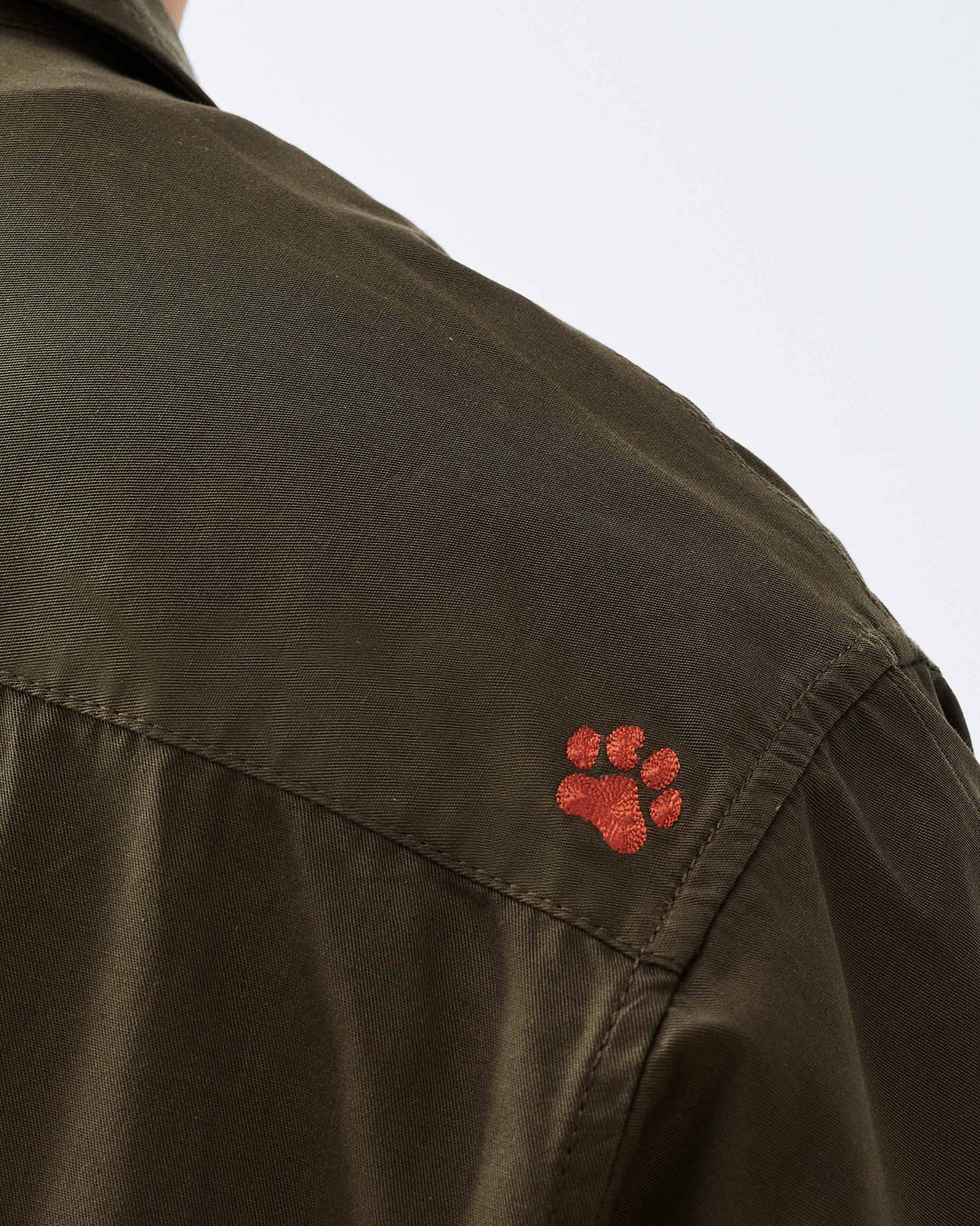 Close-up of an orange paw embroidery on an olive utility jacket.