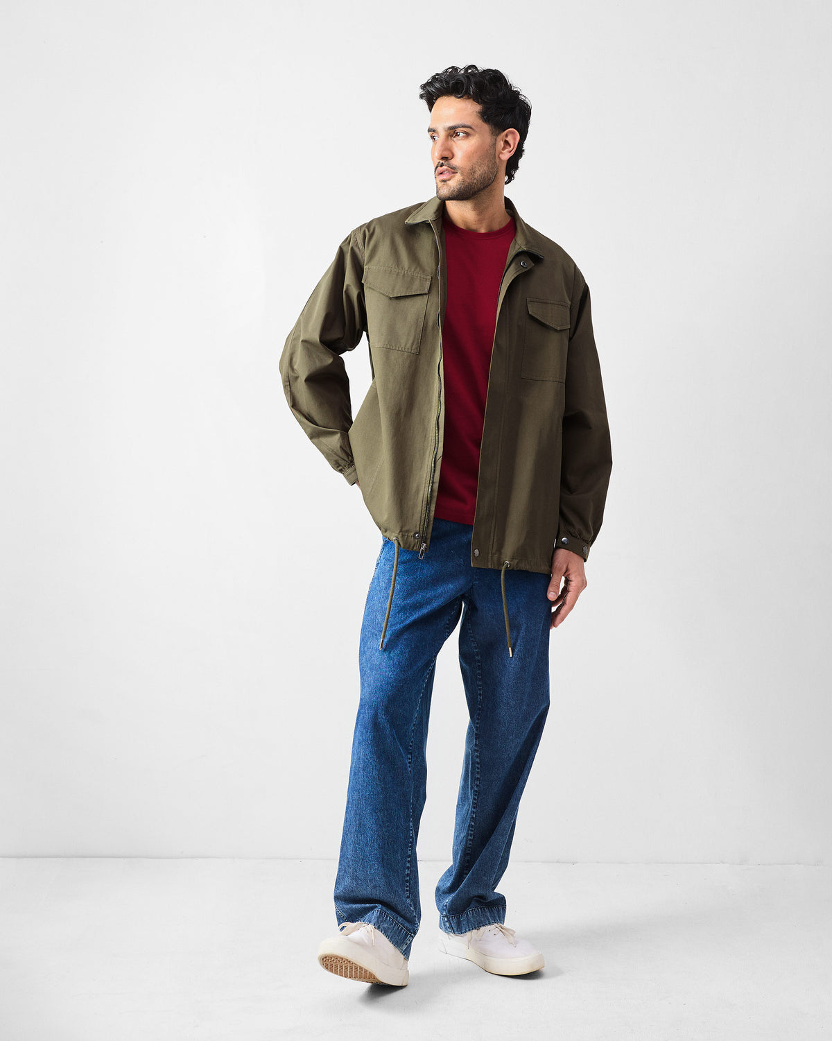 Person wearing an olive utility jacket open over a red t-shirt.