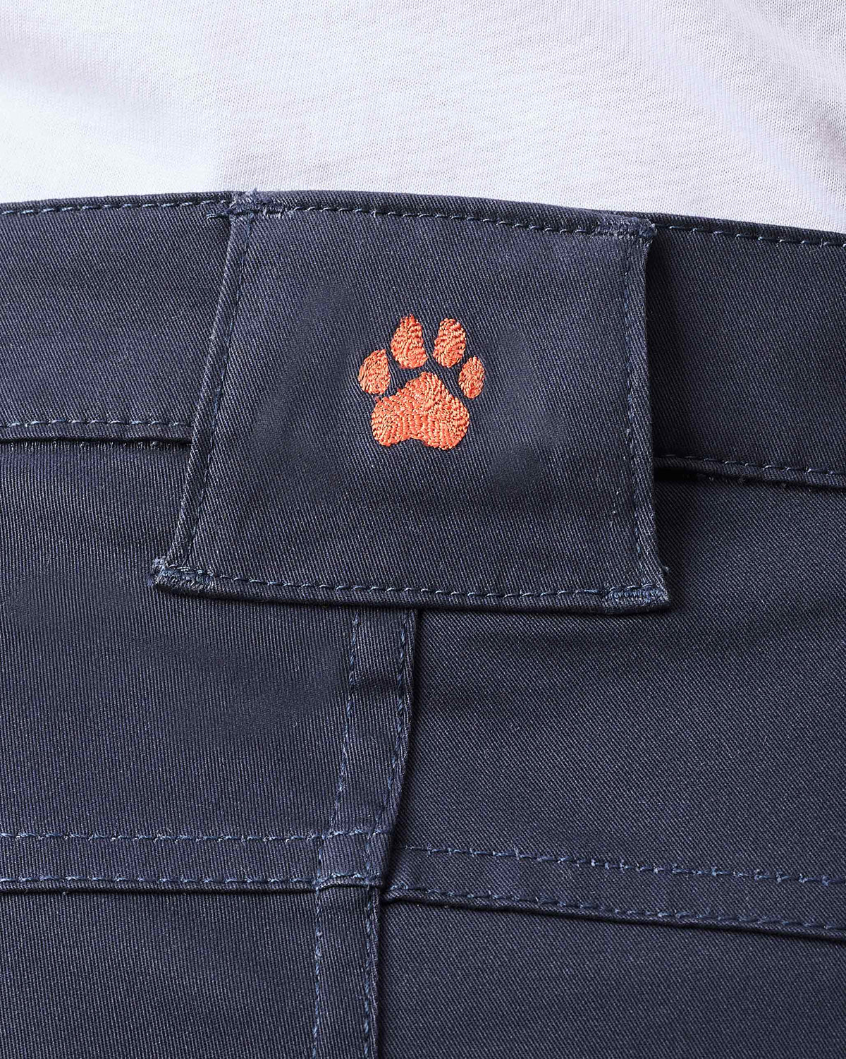 Close-up of an orange paw embroidery on the waistband of navy Boscage pants.