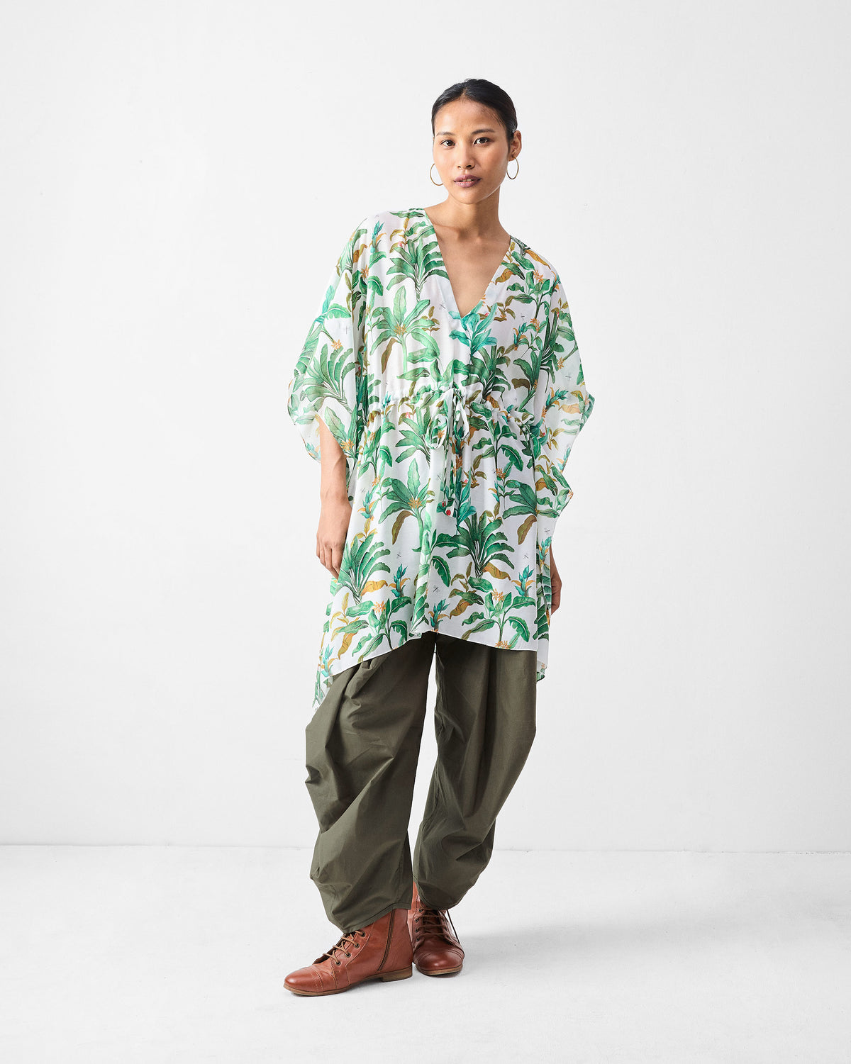 Person wearing a white Munnar Kaftan with a green palm print over trousers.