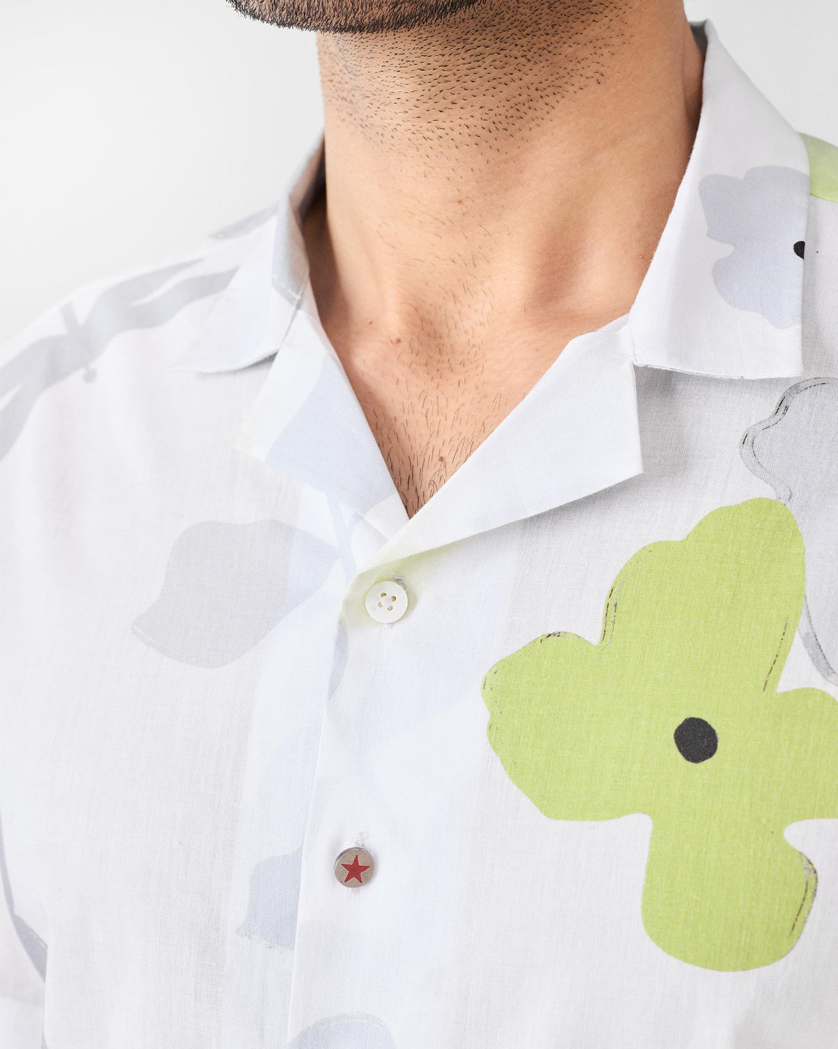 Close-up of a white Mistari Shirt showing lime floral print and a red star button.