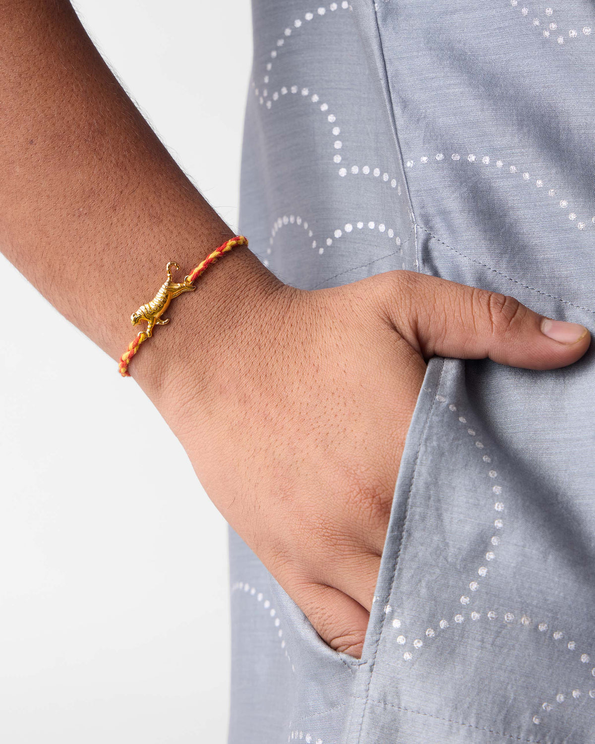 Close-up of Tiger Rakhi in red on a wrist showing its gold tiger charm.
