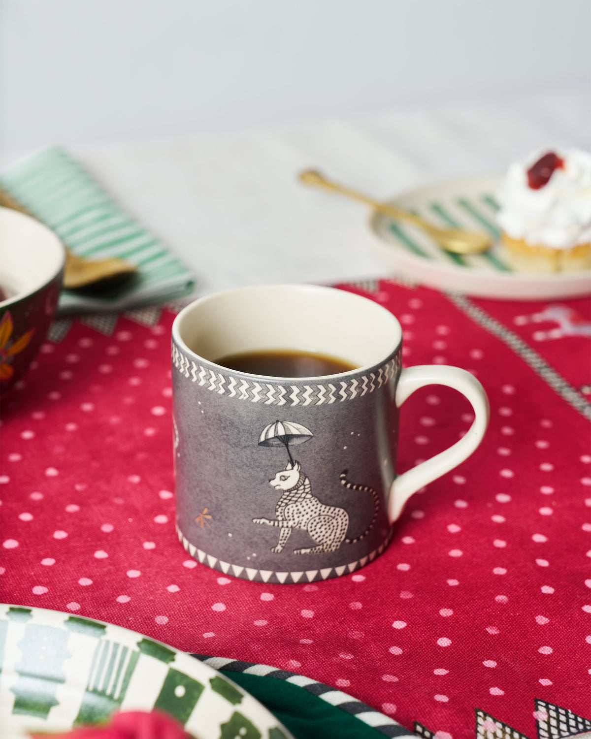 The Bagh Straight Mug with coffee on a pink tablecloth.