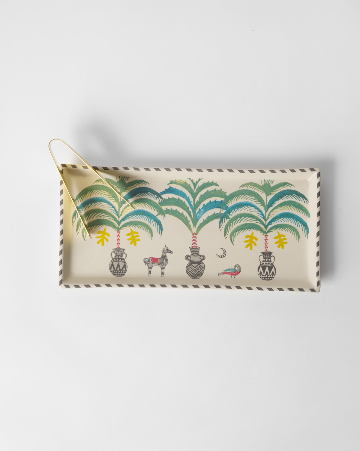 Overhead of an Indus cookie tray with teal palms, a striped rim, and gold tongs.
