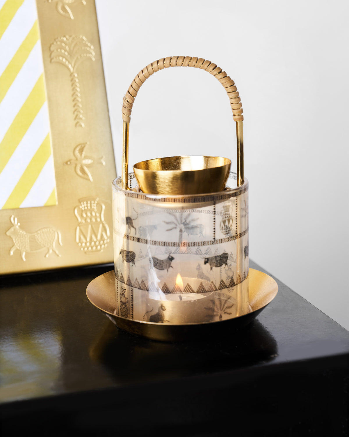 Lit Indus diffuser with rattan handle beside a matching gold frame.