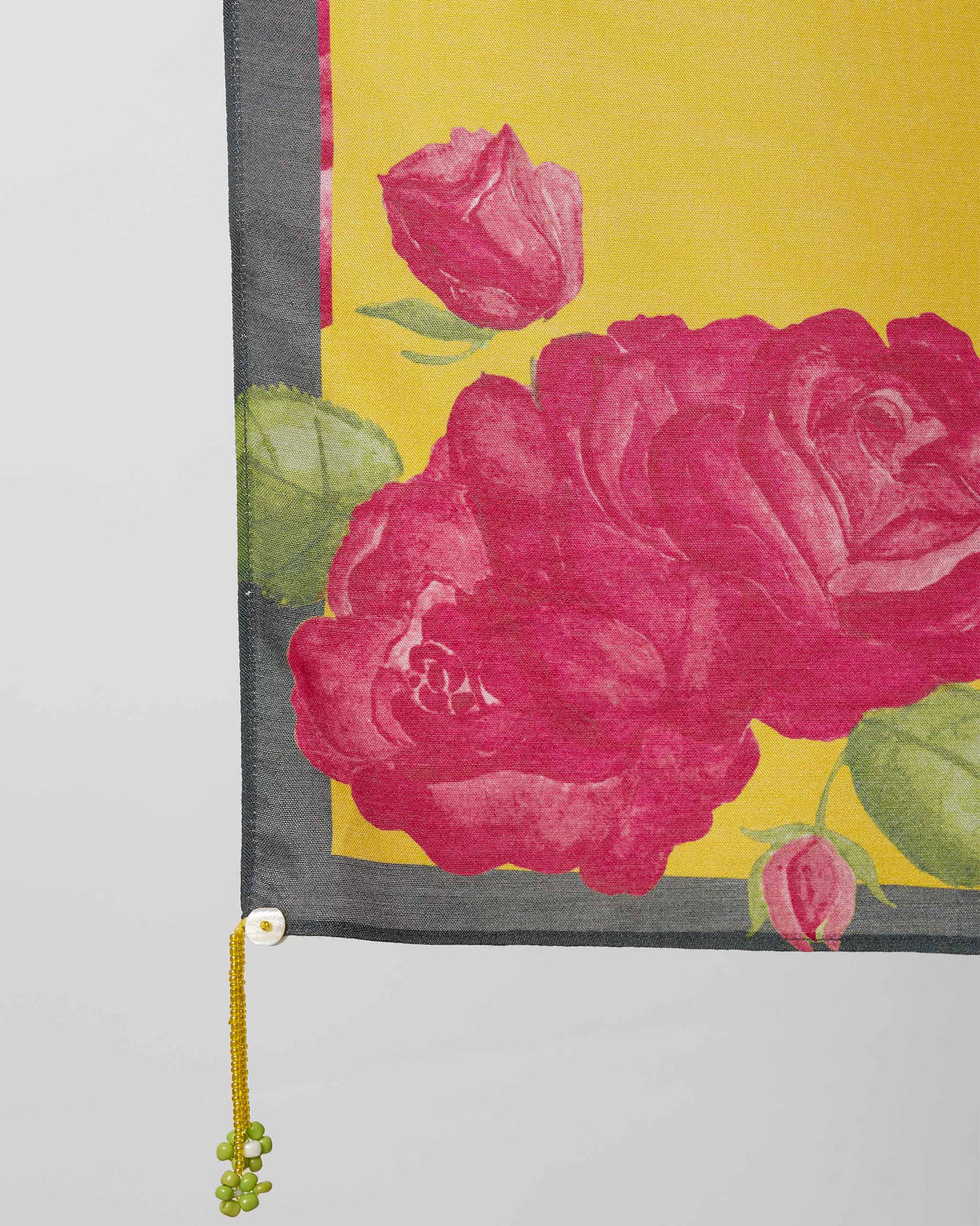 Close-up of a Kesar scarf corner showing pink roses, green leaves and a beaded tassel.